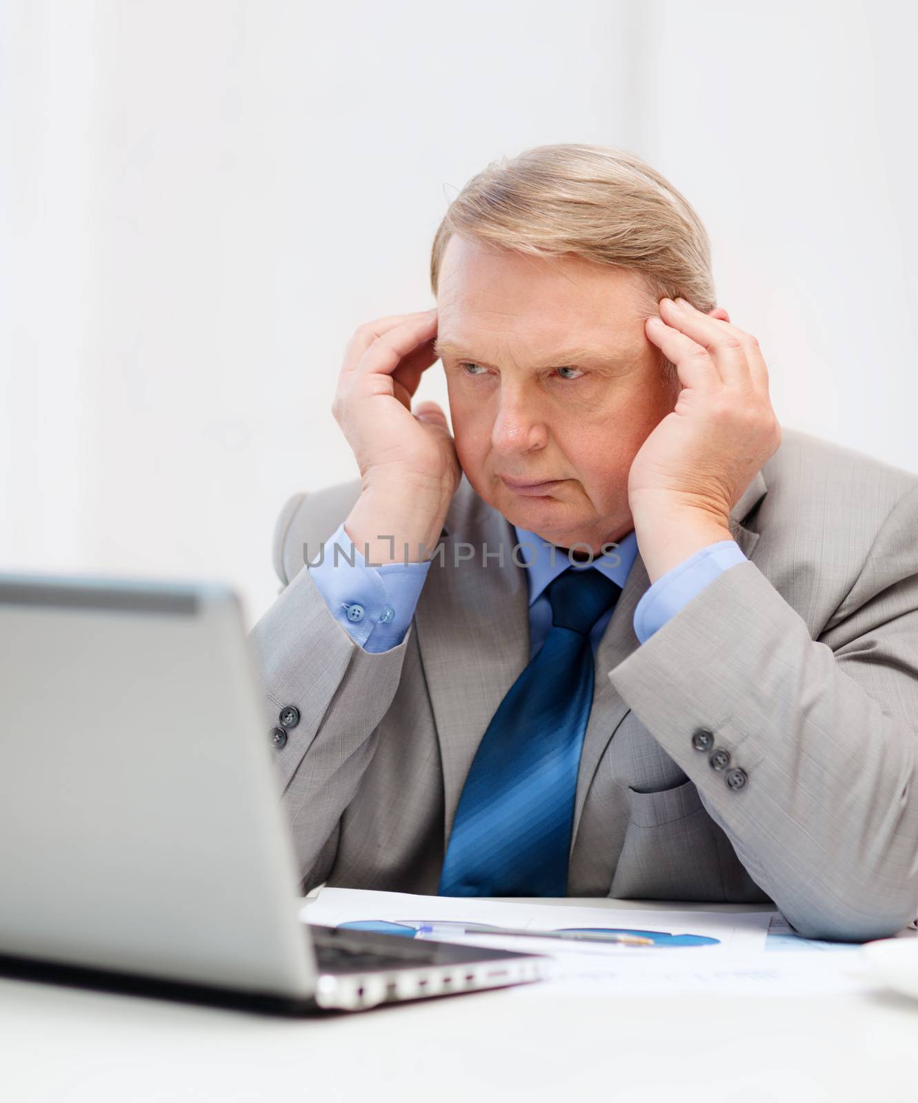 business, technology and office concept - upset older businessman with laptop and charts in office