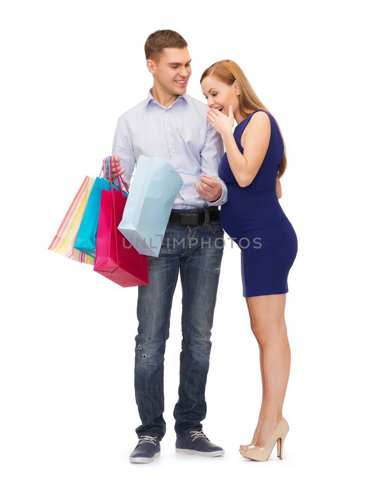 pregnancy, shopping, parenthood and happiness concept - happy young family with shopping bags expecting child pointing finger