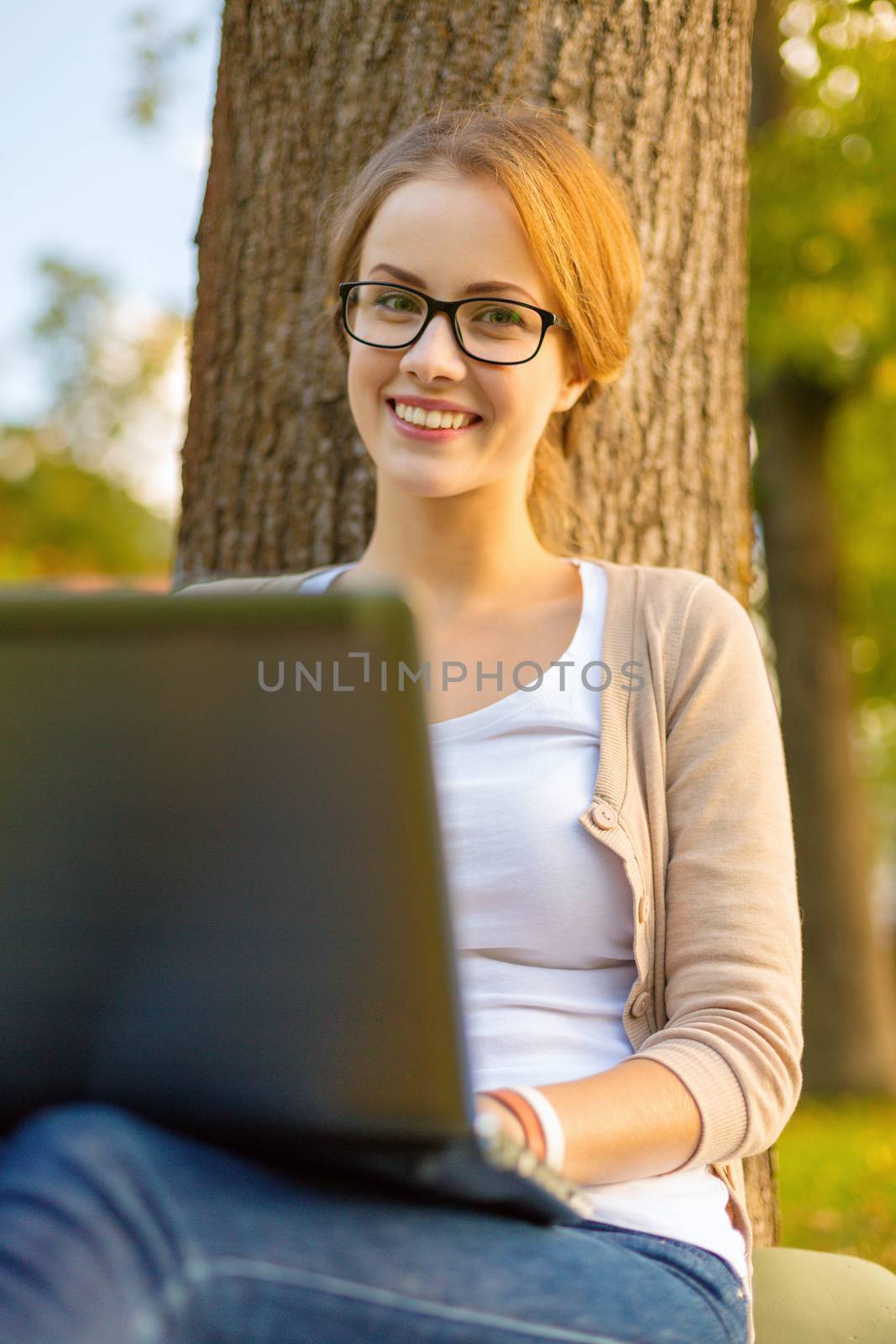 education, technology and internet concept - smiling teenager in eyeglasses with laptop computer