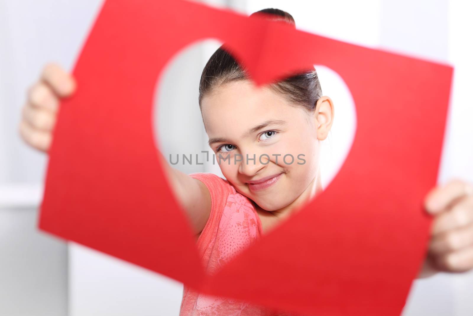 Beautiful little girl looking through the card with a heart cut out
