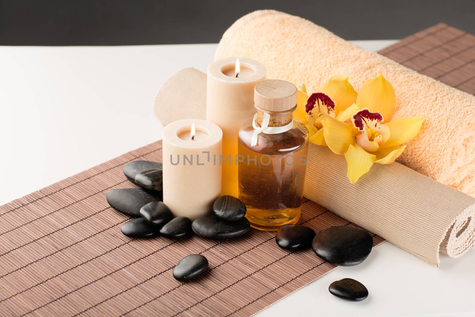 spa, health and beauty concept - closeup of essential oil, massage stones, candles and orchid flower