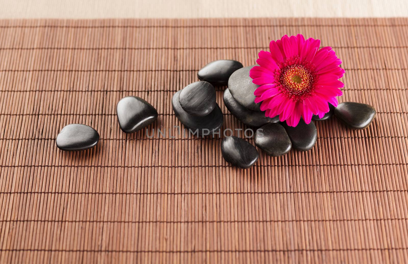 spa, heath and beauty concept - massage stones with flower on mat