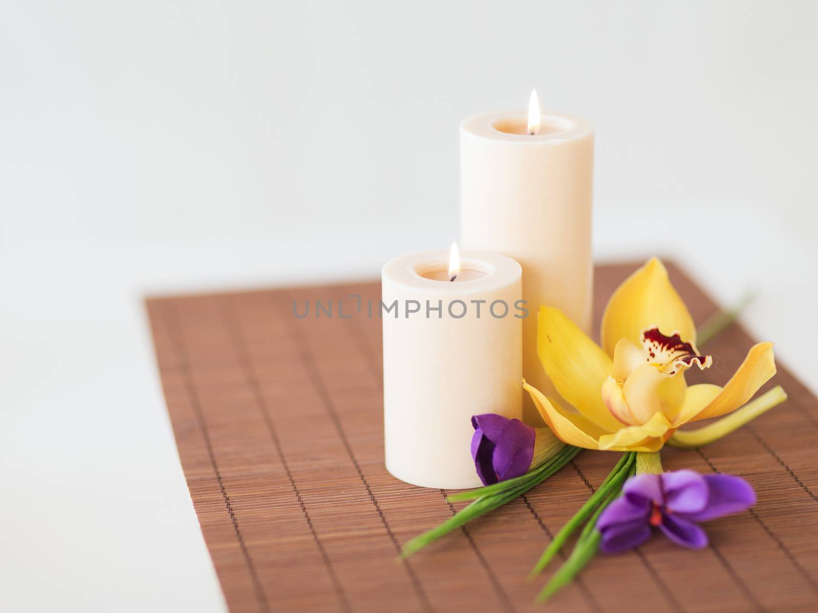 spa, health and beauty concept - candles, orchid and iris flowers on bamboo mat