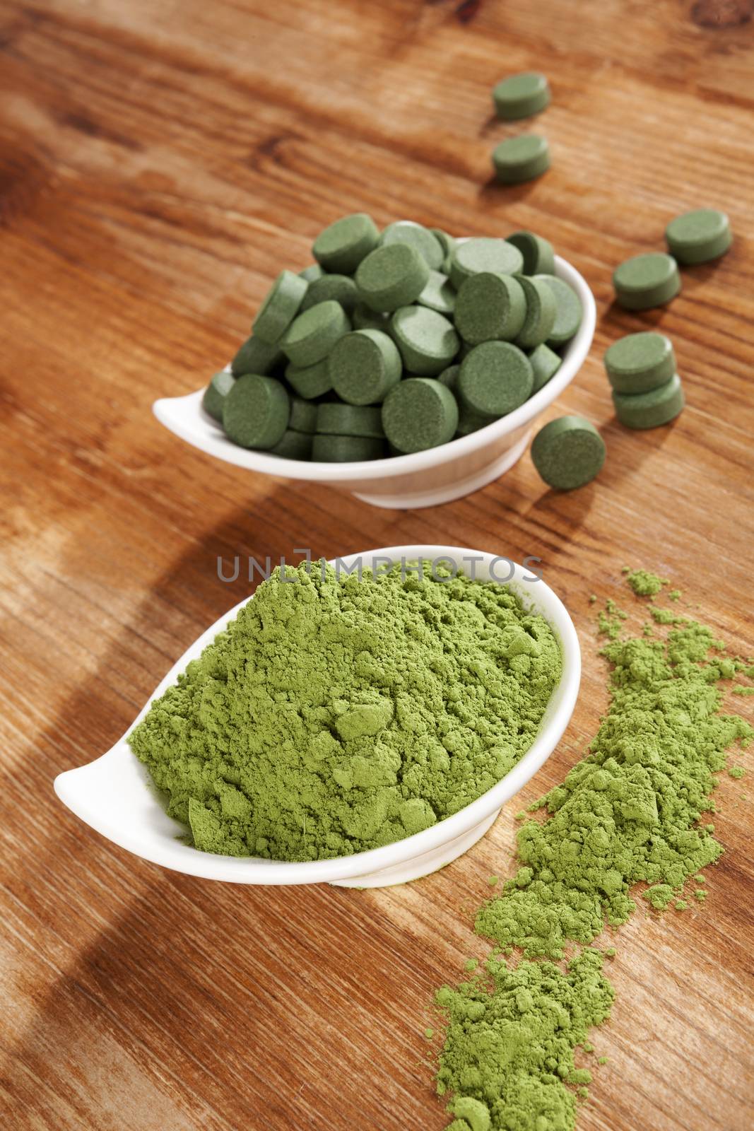 Chlorella pills and wheat grass powder in bowl on brown wooden background. Natural alternative medicine, weight loss and detox.
