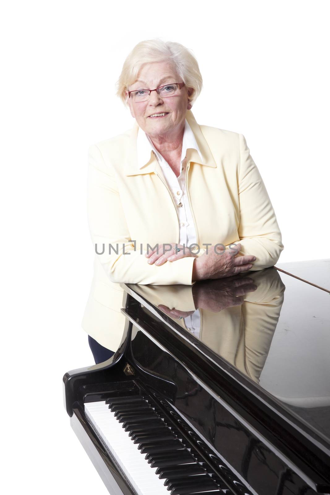elderly lady in yellow leaning on grand piano in studio with white background