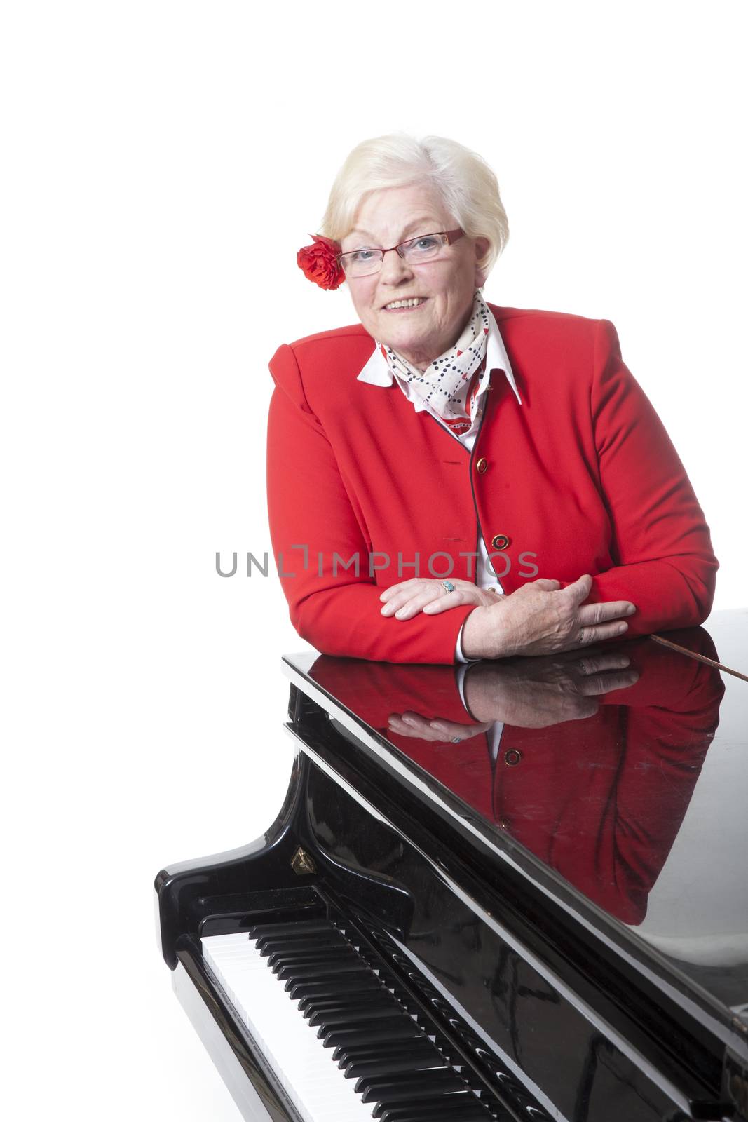 elderly lady in red leaning on grand piano in studio with white background