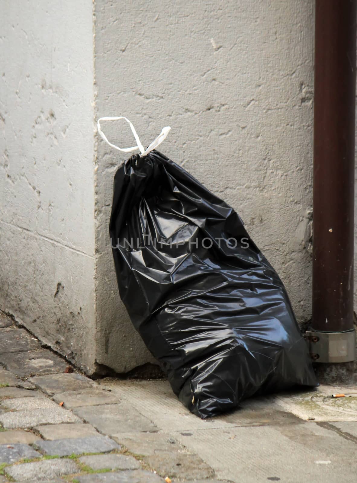 One black garbage bag in the street against a wall