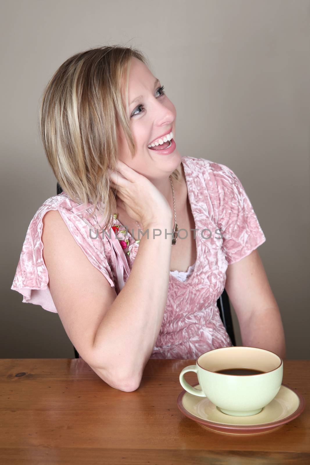 Beautiful blond woman sitting by a table drinking coffee