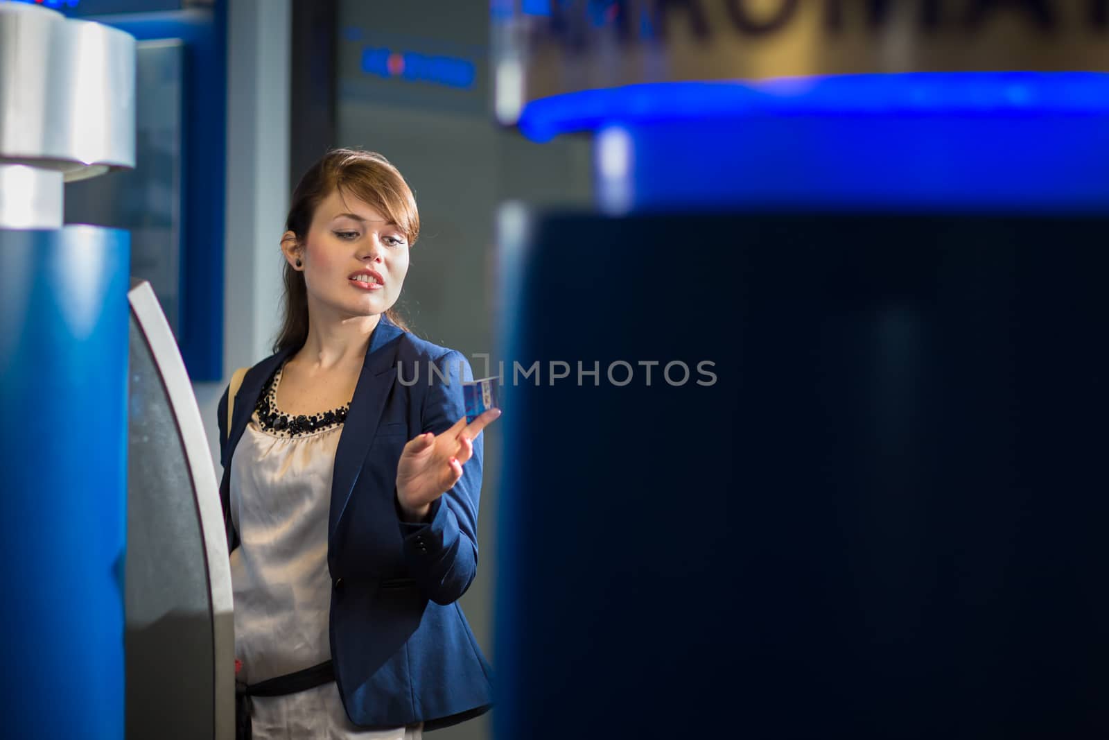 Pretty, young woman withdrawing money from her credit card in at an ATM (shallow DOF; color toned image)