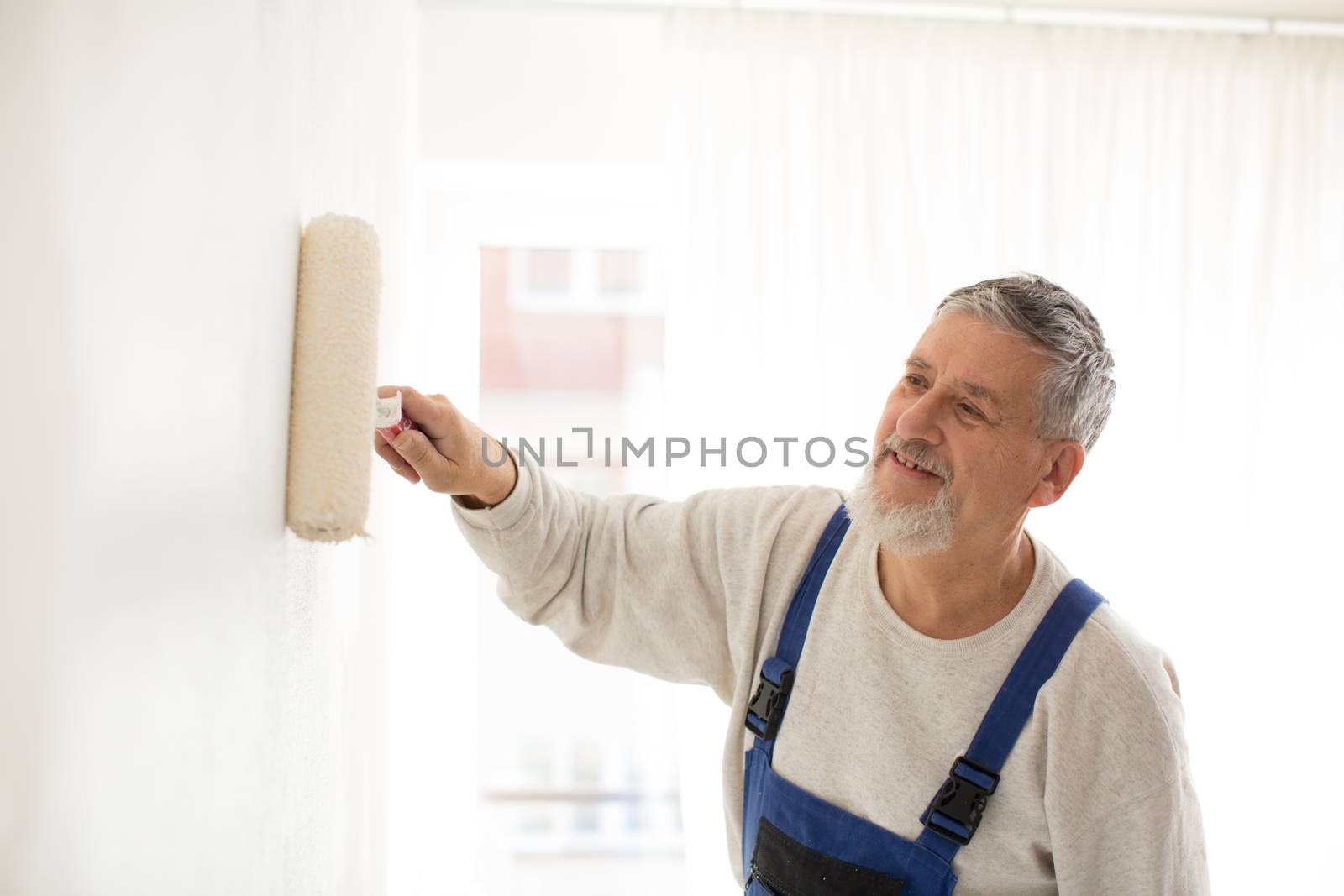 Senior man painting a wall in with paint roller, smiling, enjoying the work