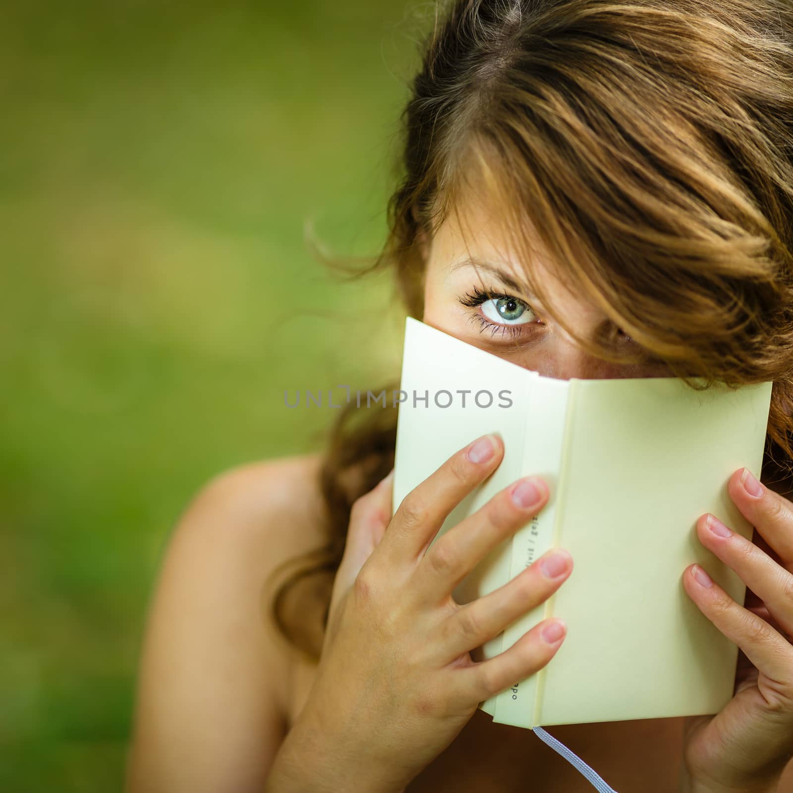 Cute young woman  covering her face with a book she is reading