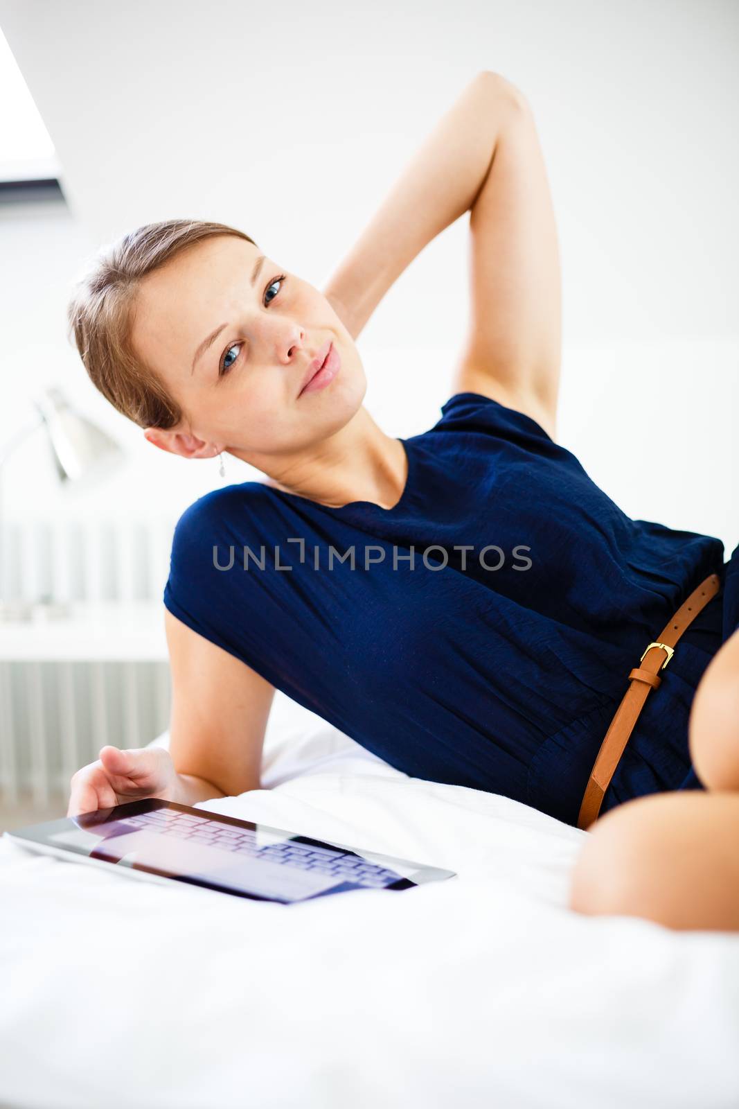 Pretty, young woman using her tablet computer in bed, after coming home from work (shallow DOF; color toned image)