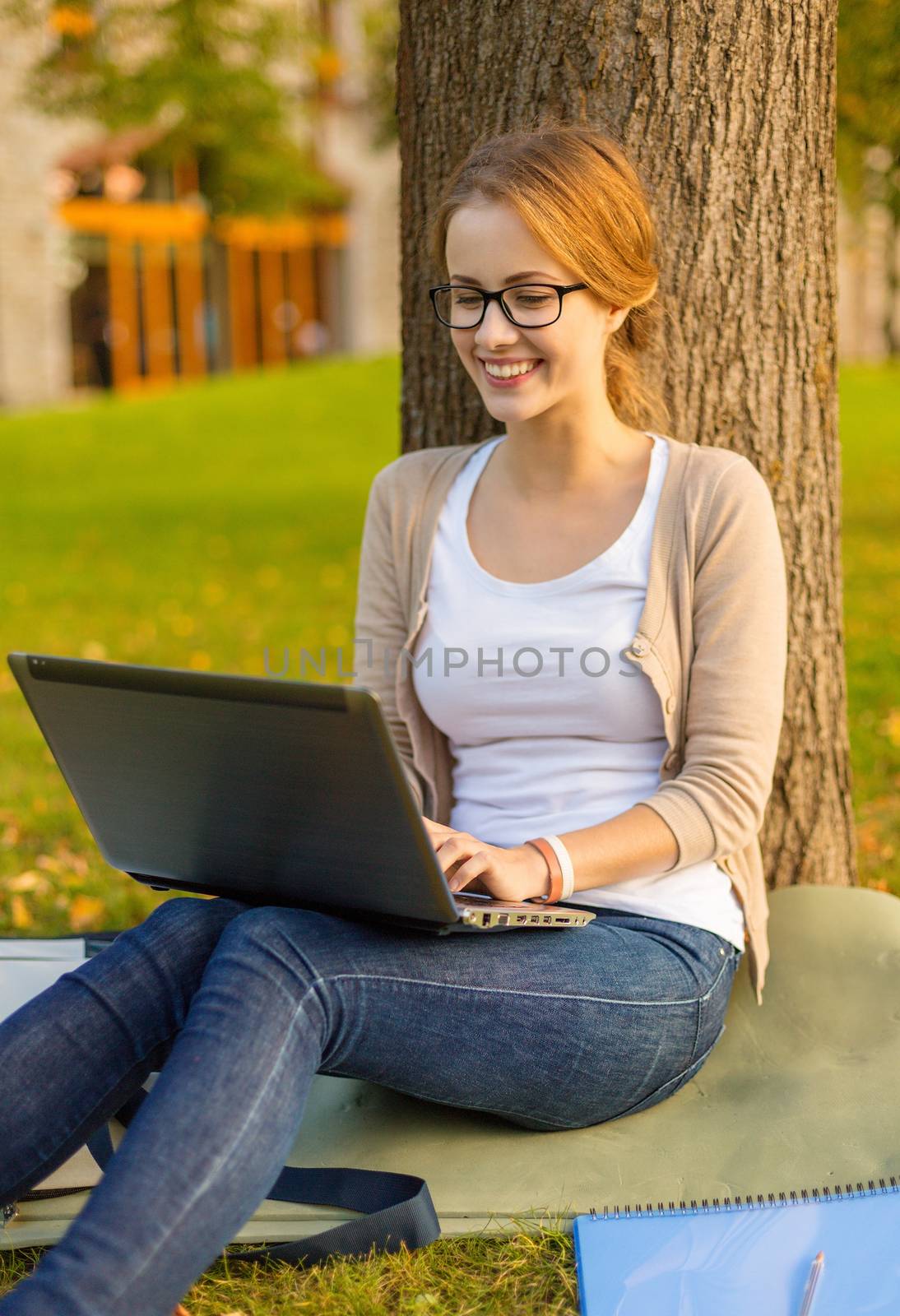 education, technology and internet concept - smiling teenager in eyeglasses with laptop computer and notebook