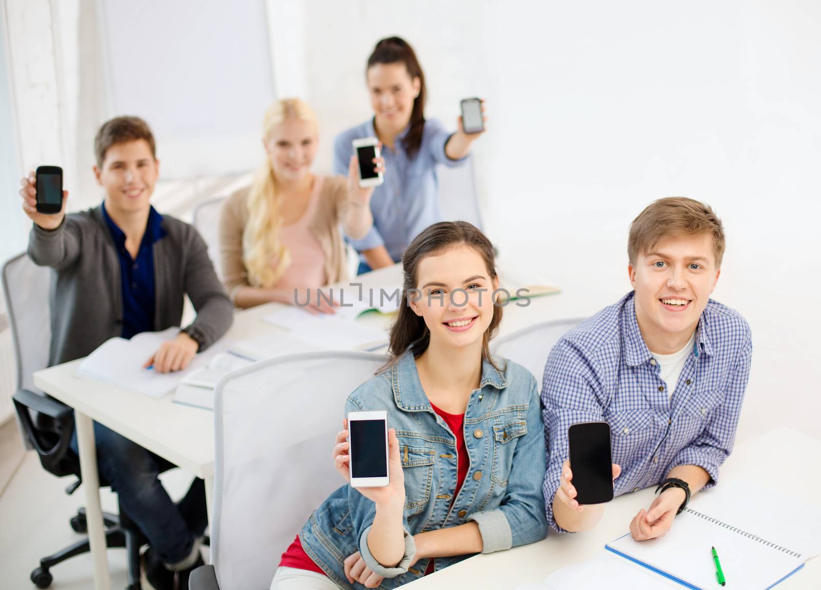 education, school, technology and internet concept - smiling students showing black blank smartphone screens at school