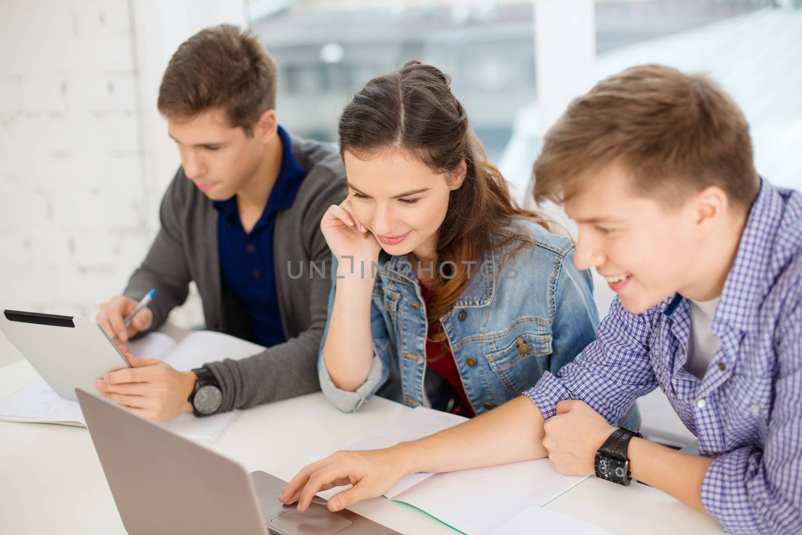 education, technology, school and internet concept - three smiling students with laptop, tablet pc and notebooks at school