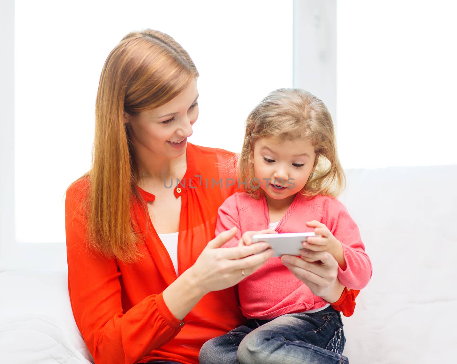 family, children, parenthood, technology and internet concept - happy mother and daughter with smartphone at home