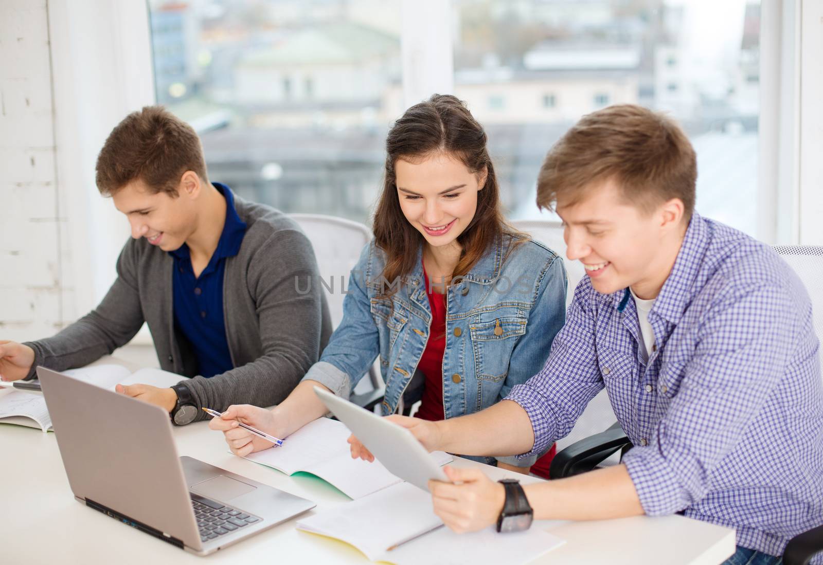 education, technology, school and internet concept - three smiling students with laptop, tablet pc and notebooks at school