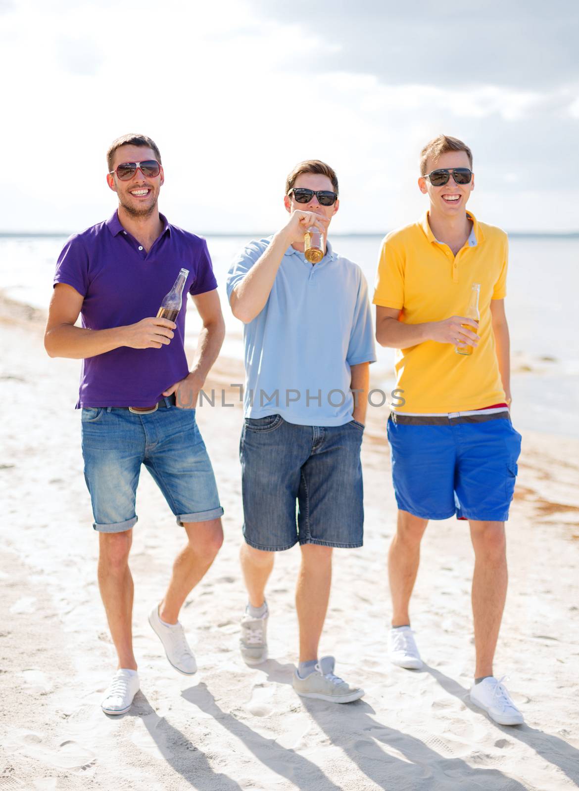 summer, holidays, vacation and people concept - group of male friends having fun on the beach with bottles of beer or non-alcoholic drinks