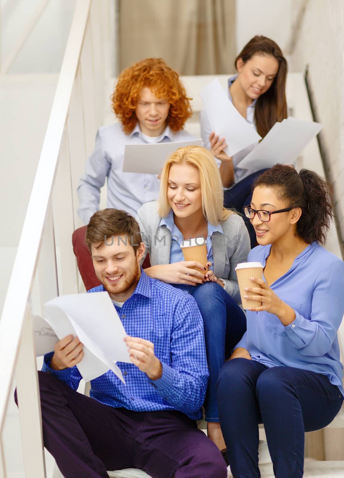 business, office and startup concept - smiling creative team with papers and take away coffee on staircase