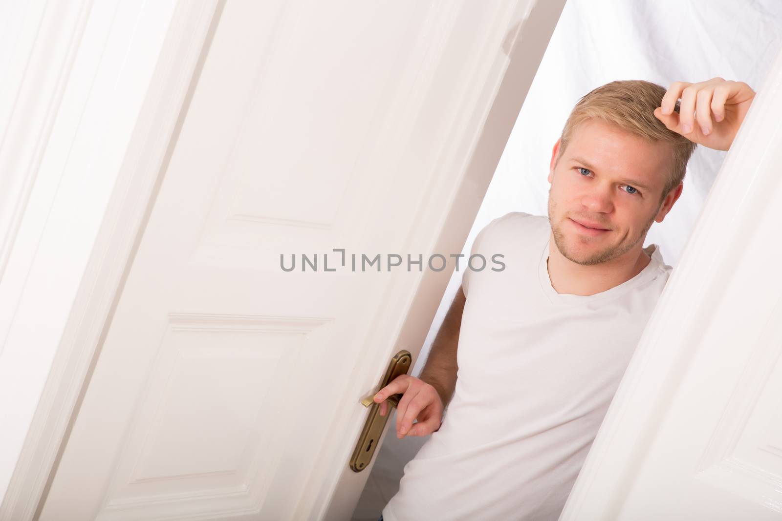 A young blonde man coming home passing through the door.