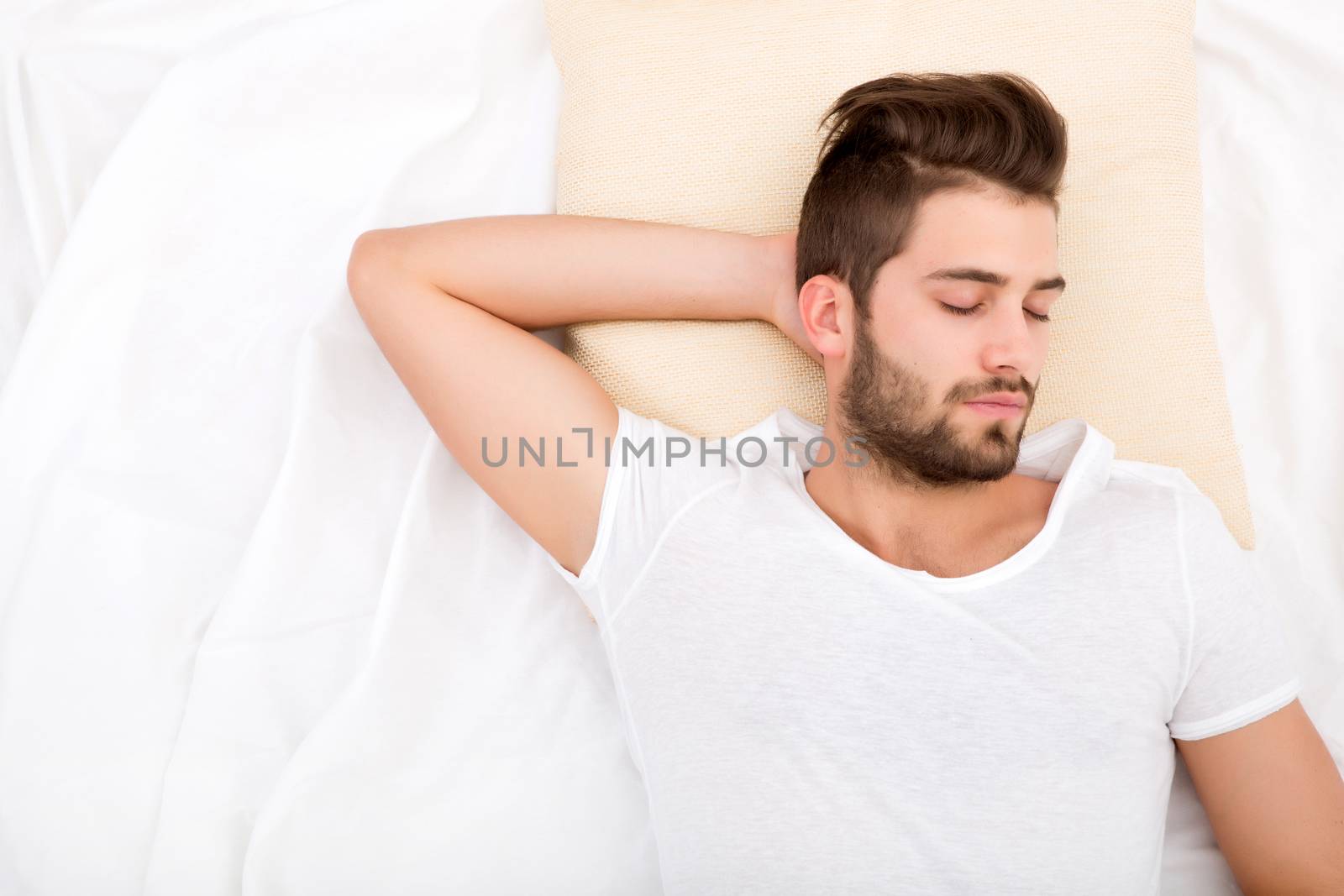 A handsome young adult man sleeping in bed.