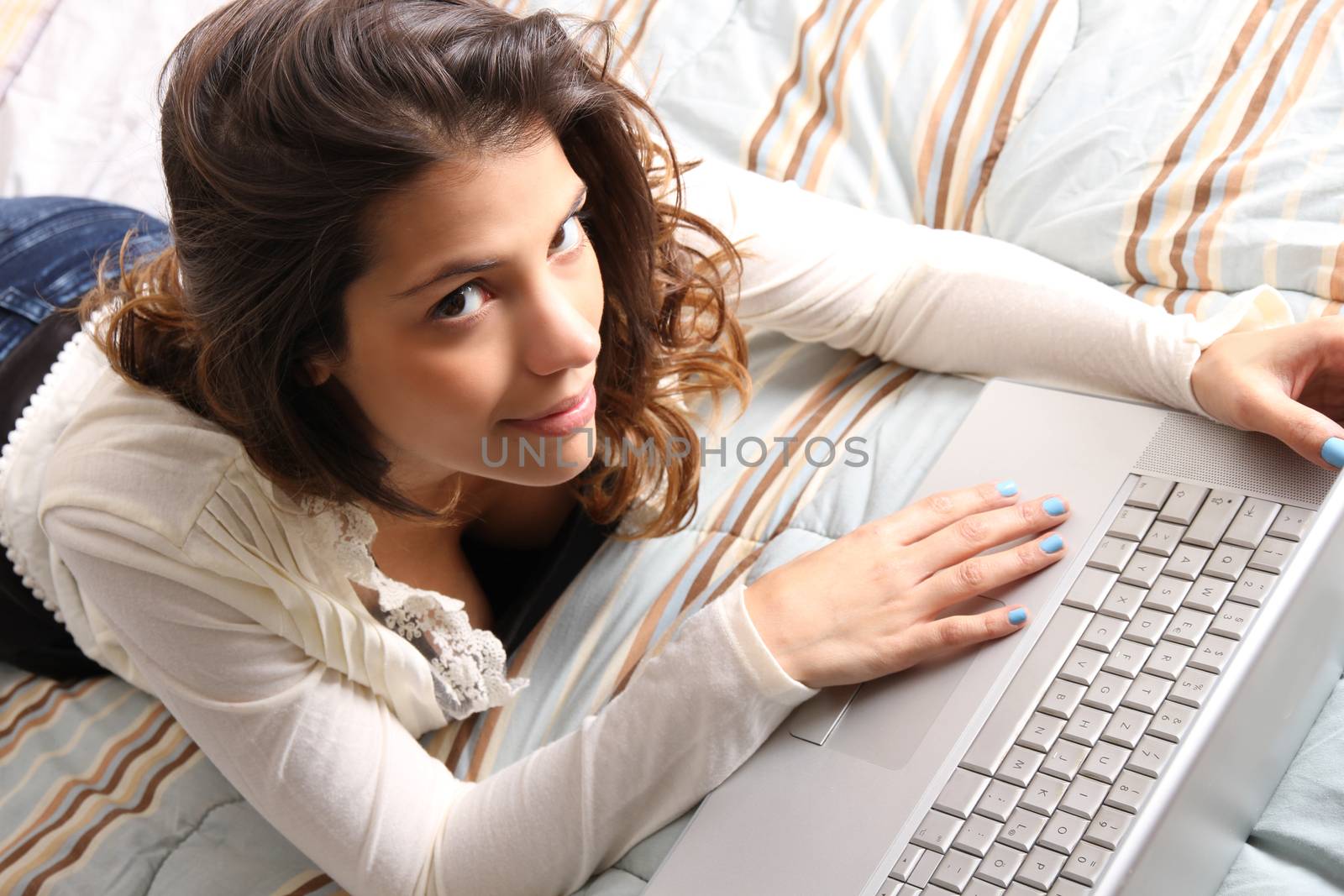 A young girl laying on the bed and surfing on the Internet with a Laptop.  