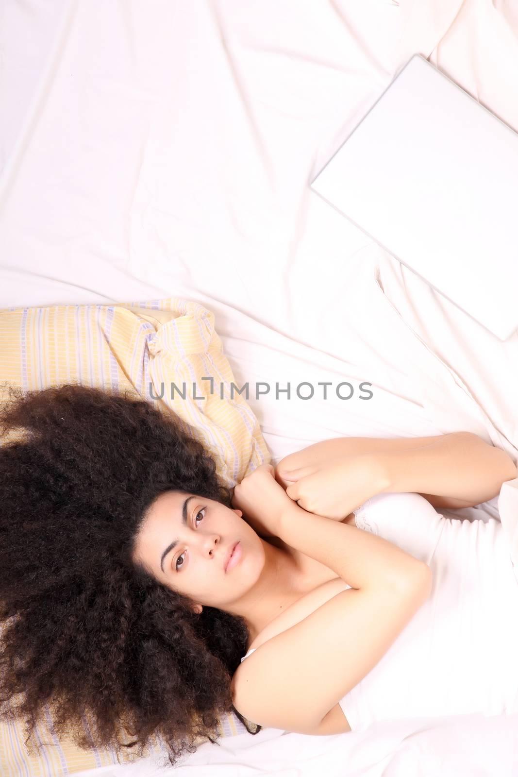 A young latin woman lying in bed with a laptop.