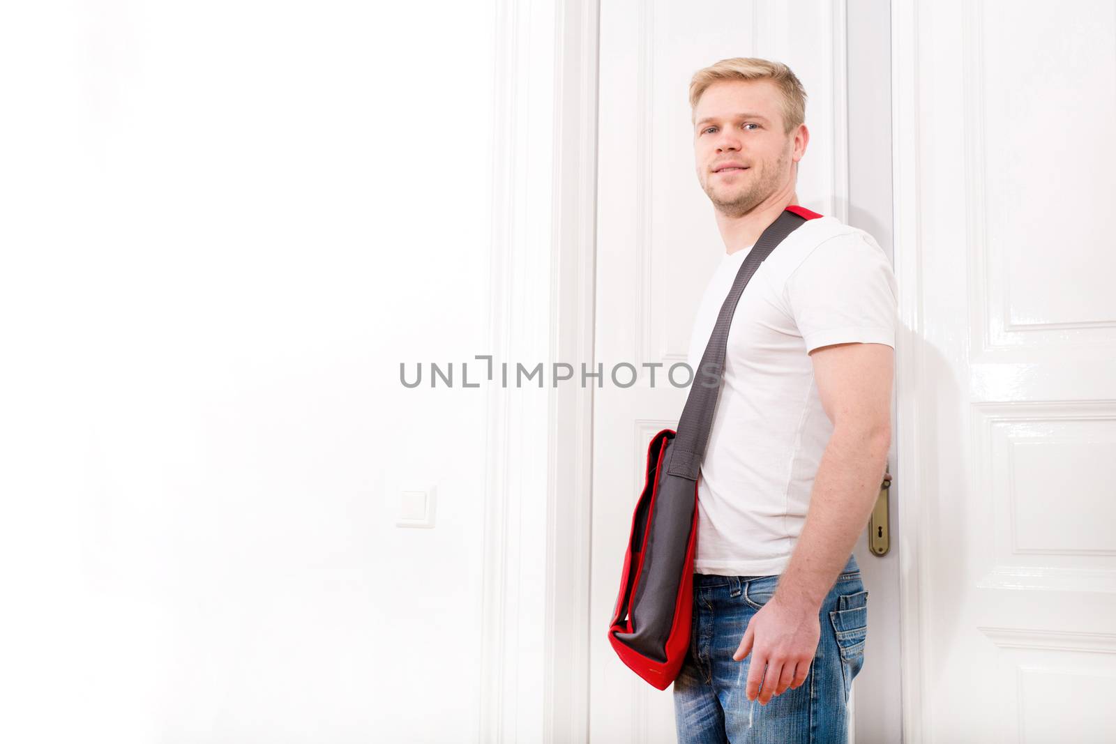 A young blonde man coming home passing through the door.