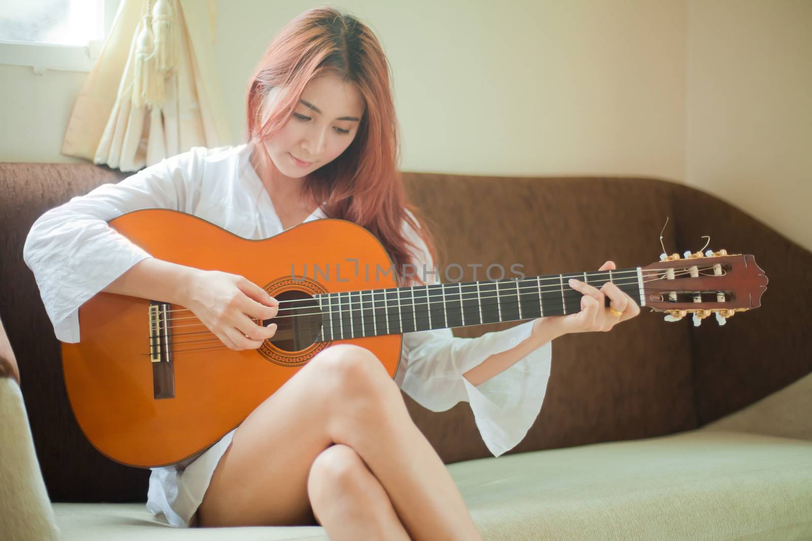 Young beautiful asian woman playing guitar in living room