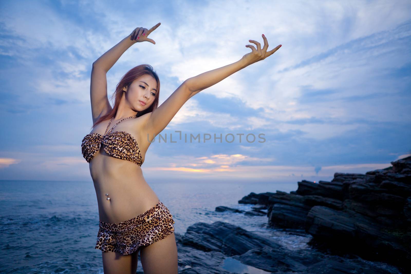 Sexy asian model posing at the stone on sunset