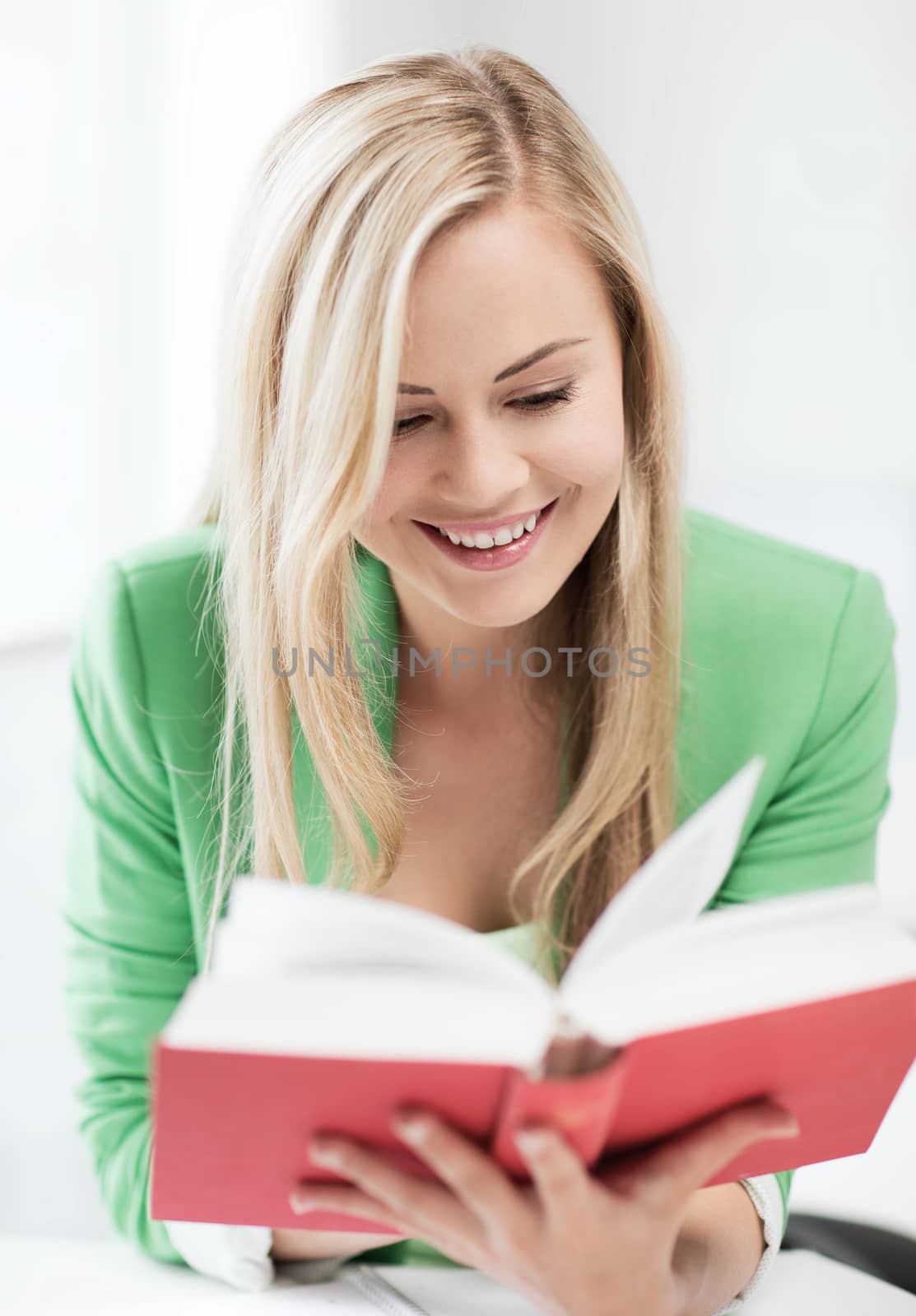 smiling young woman reading book at school by dolgachov