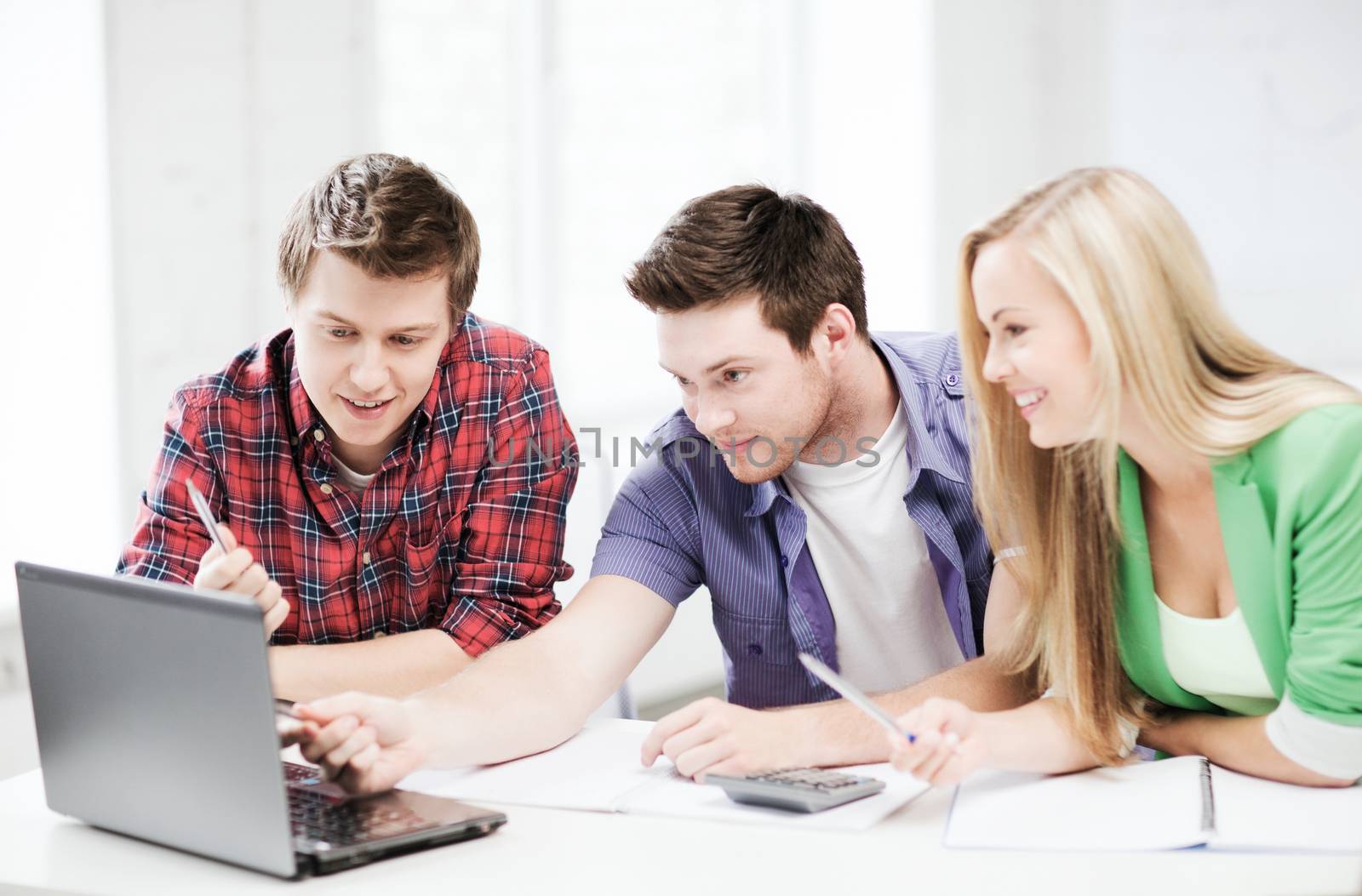 smiling students looking at laptop at school by dolgachov