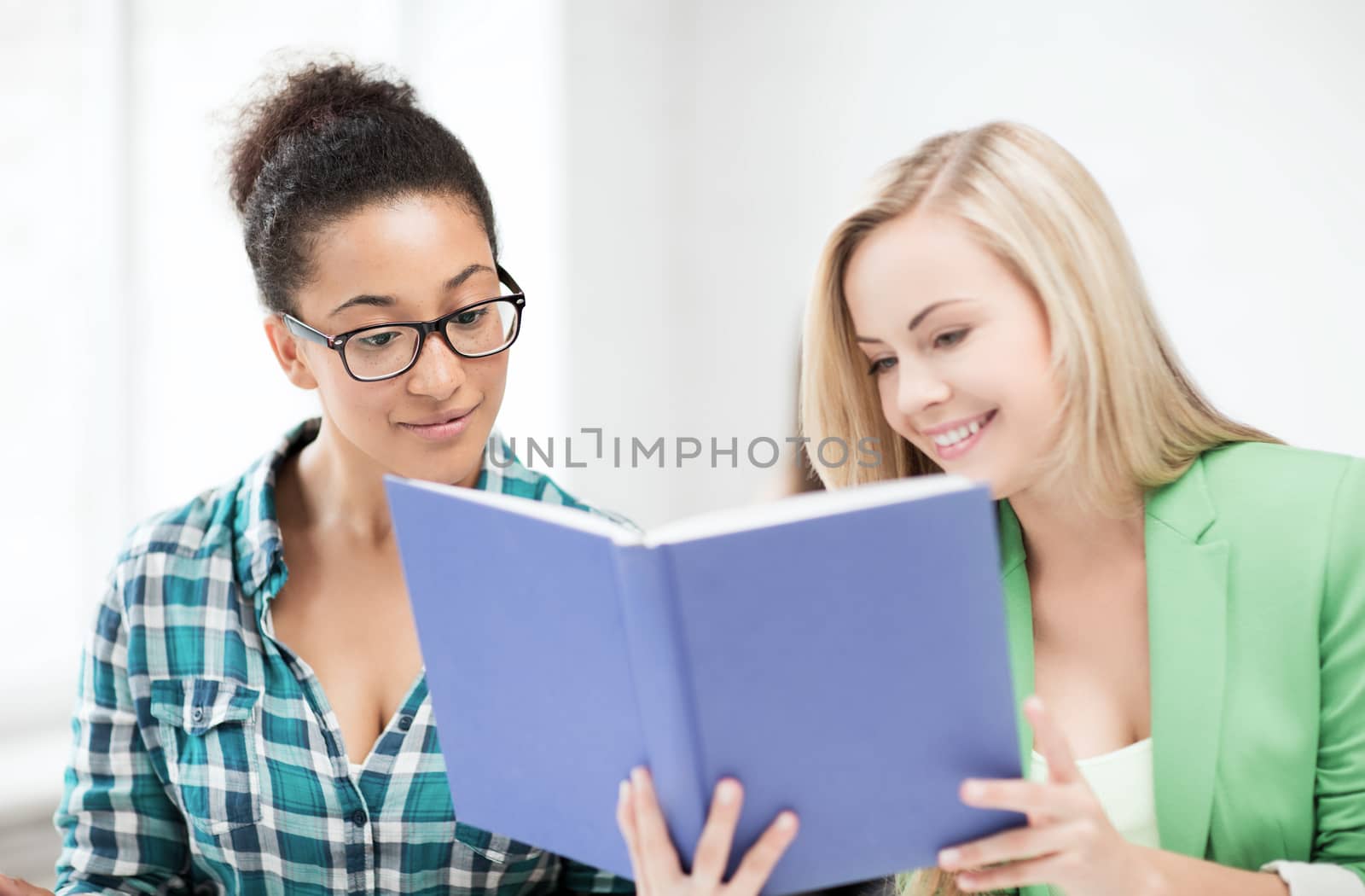 smiling student girls reading book at school by dolgachov
