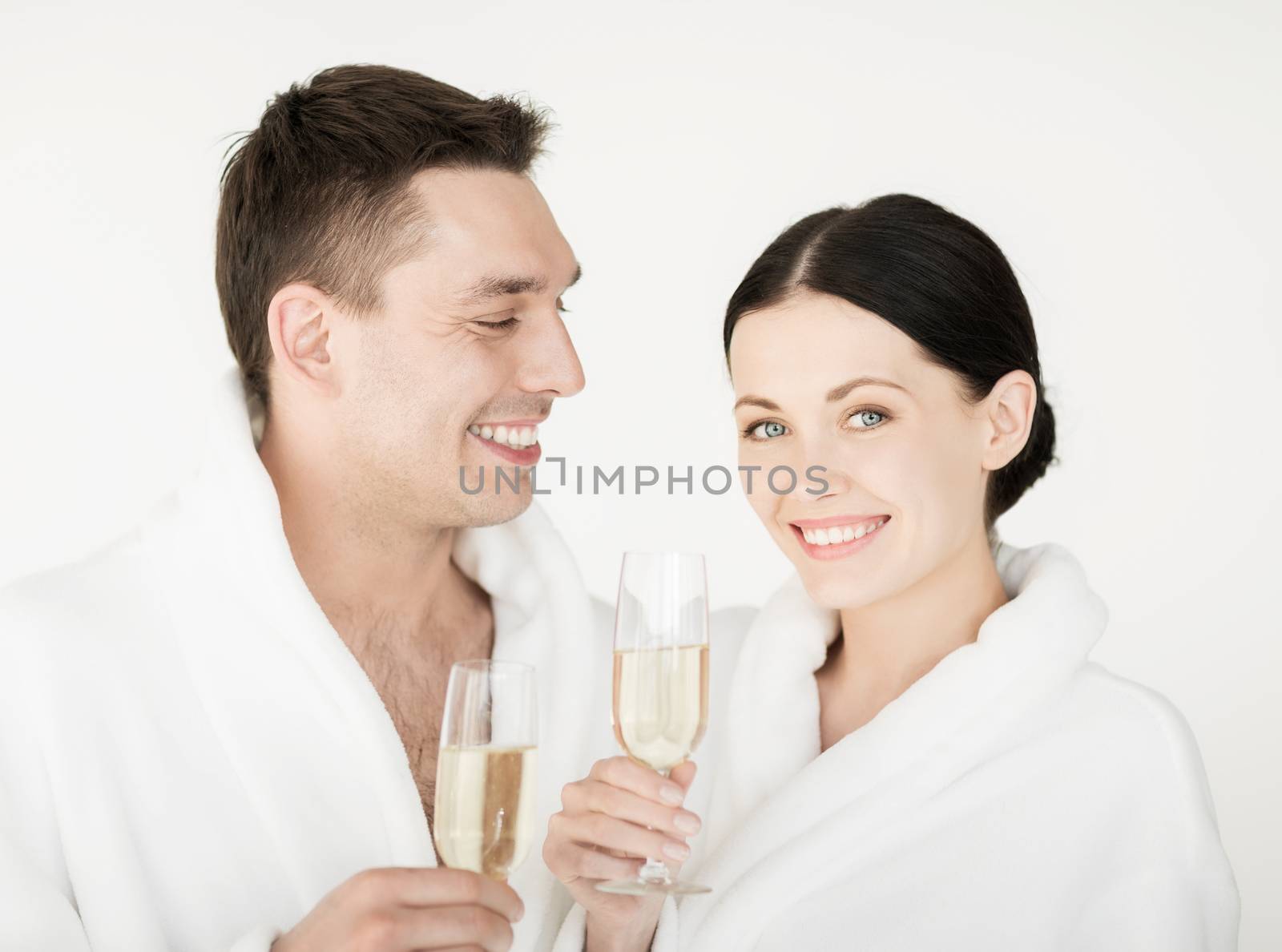 healthcare and beauty concept - picture of couple in spa salon in white bathrobes with champagne