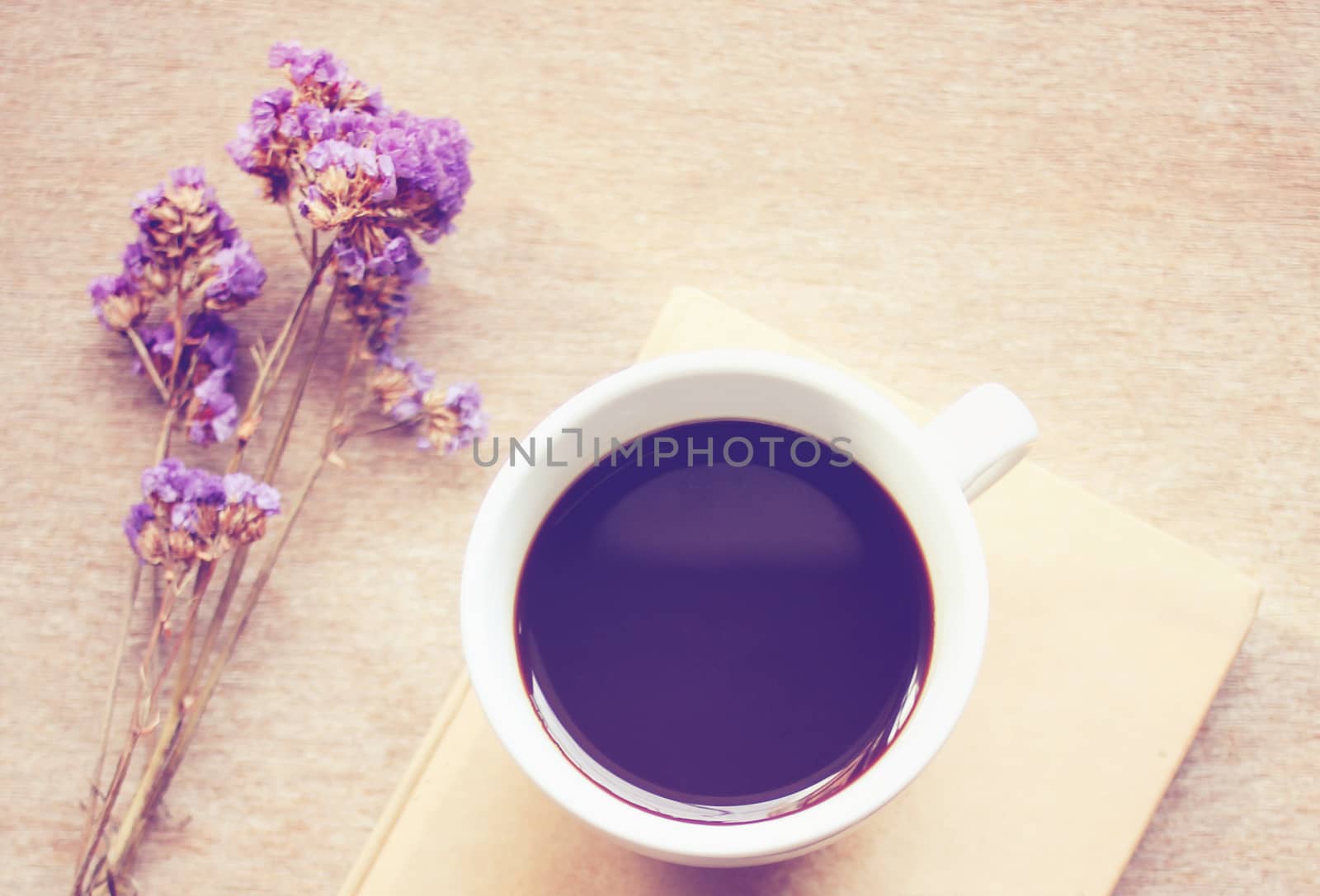 Black coffee on notebook with statice flowers, retro filter effect