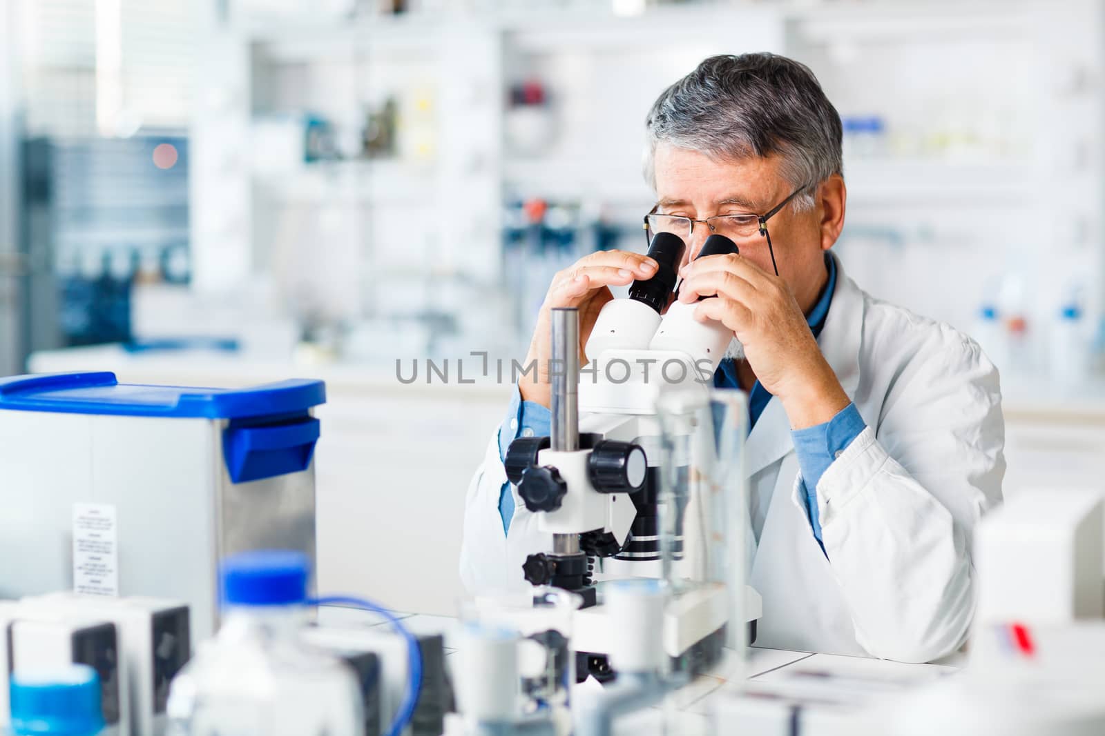 senior male researcher carrying out scientific research in a lab using a microscope (shallow DOF; color toned image)