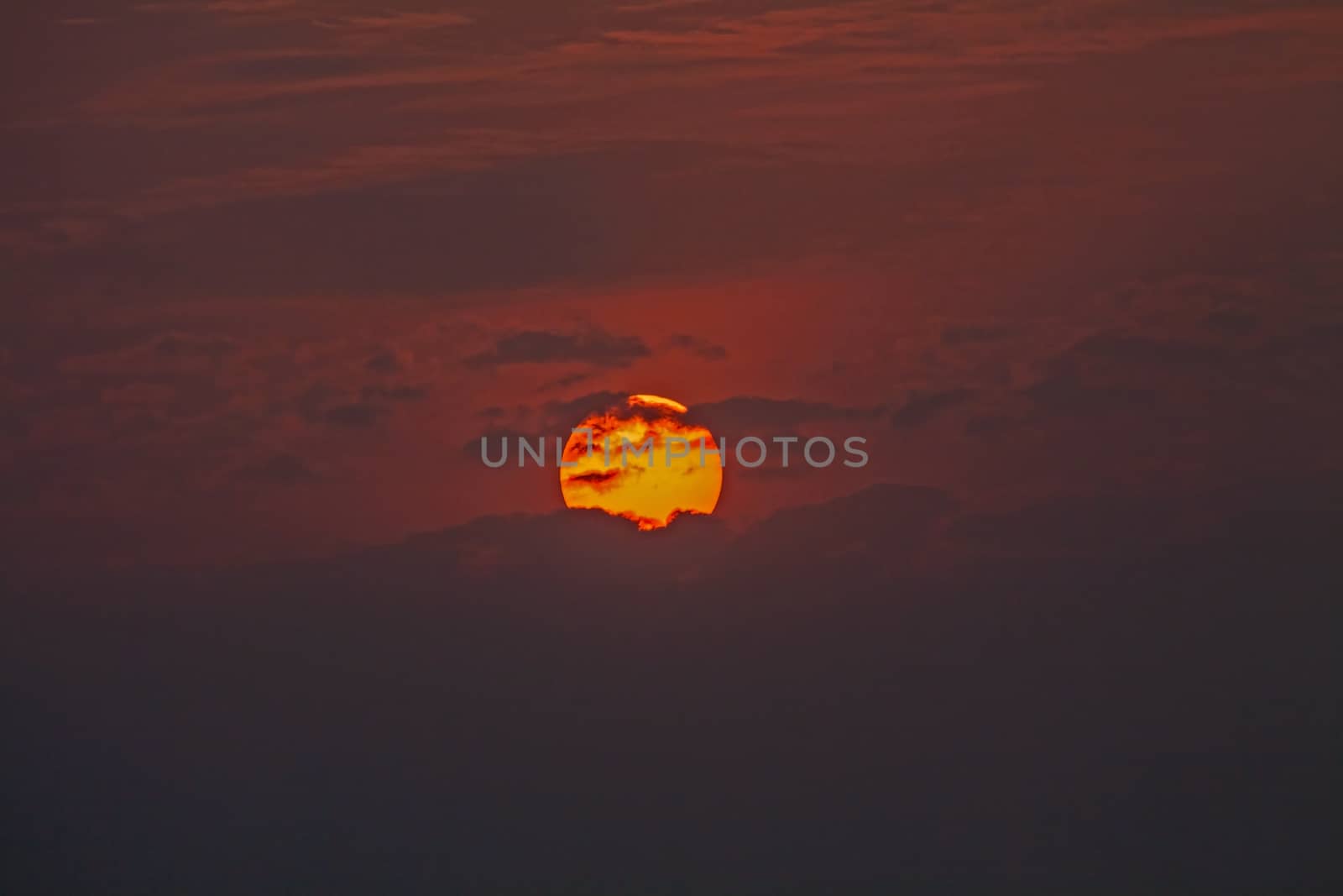 The Orange Globe of Setting Sun is partially hidden by the clouds which seem to float in front in this tropical sunset scene.