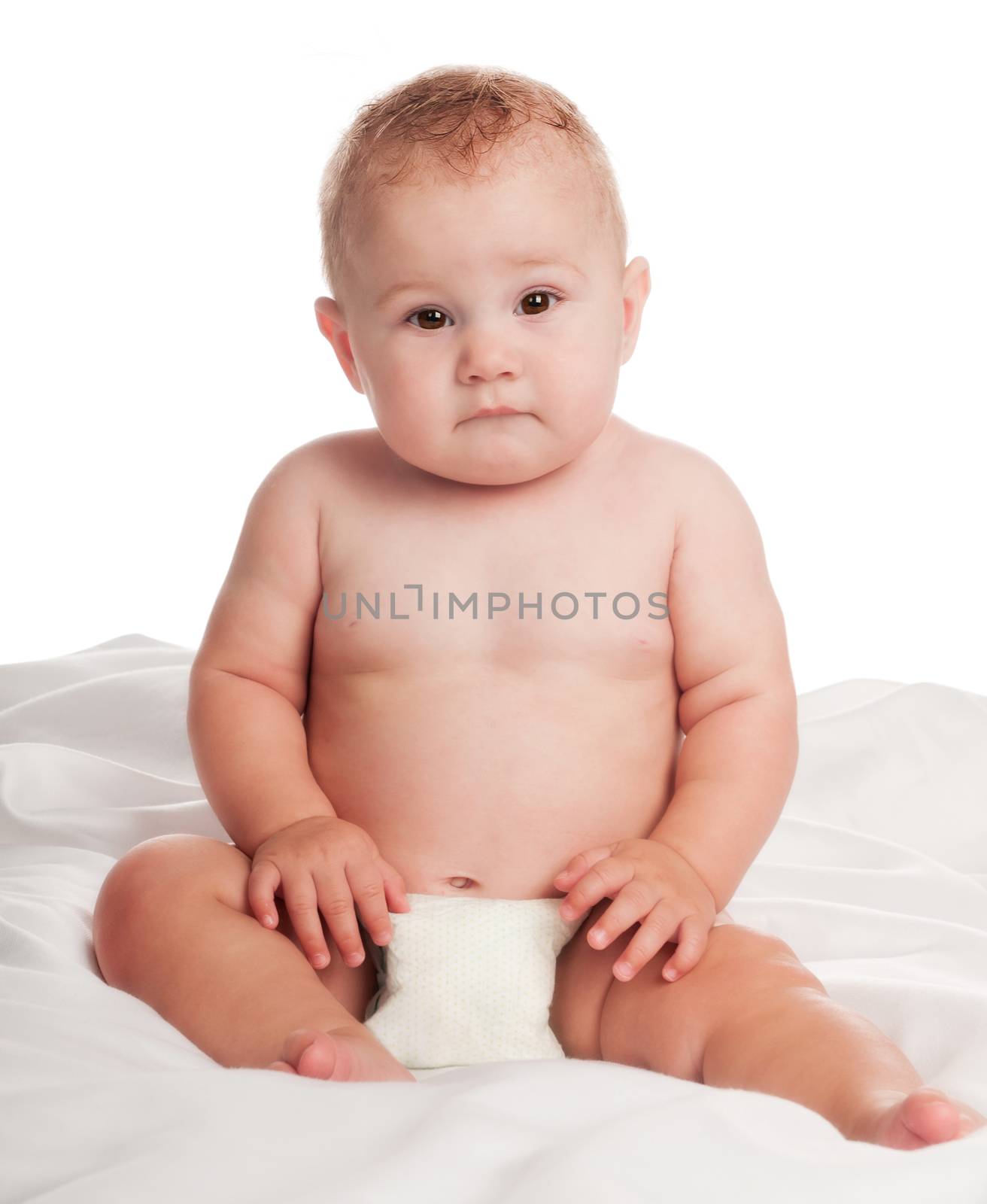 Little boy sitting on a bed in a diaper. Isolated on white