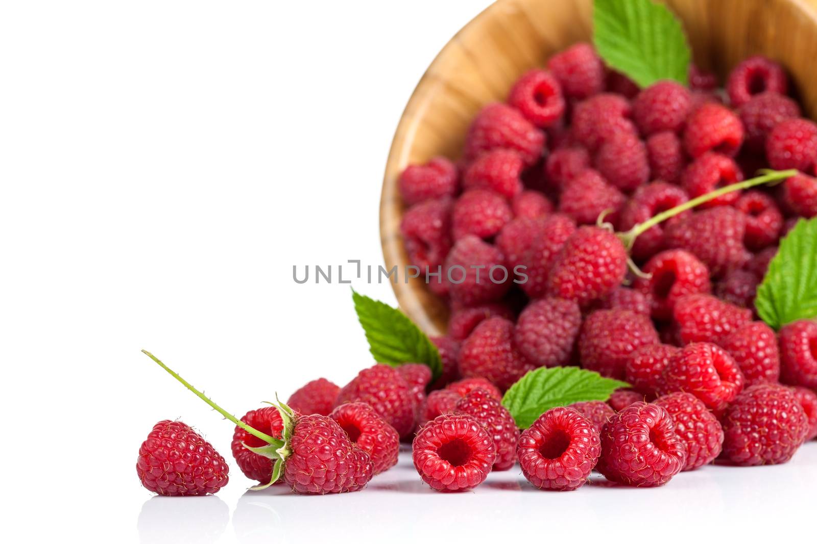 Raspberries with leaves in wooden bowl on white background