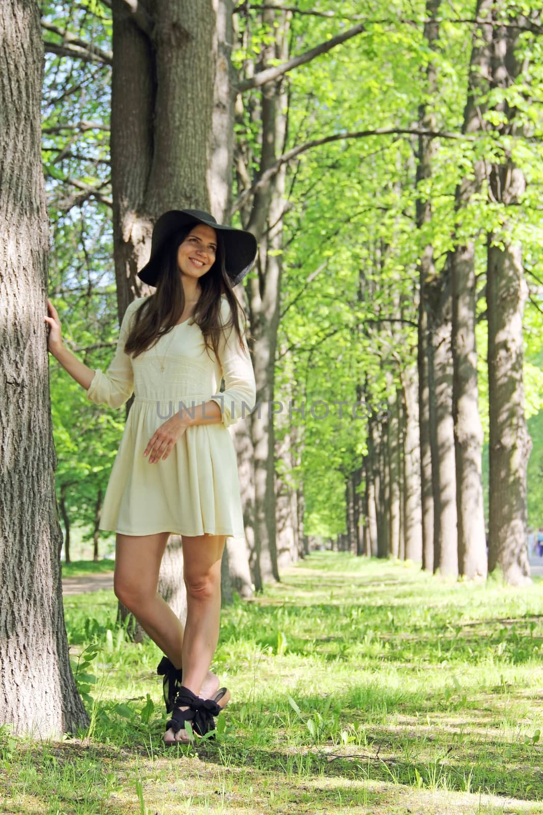 Beautiful young woman in hat walking in spring alley