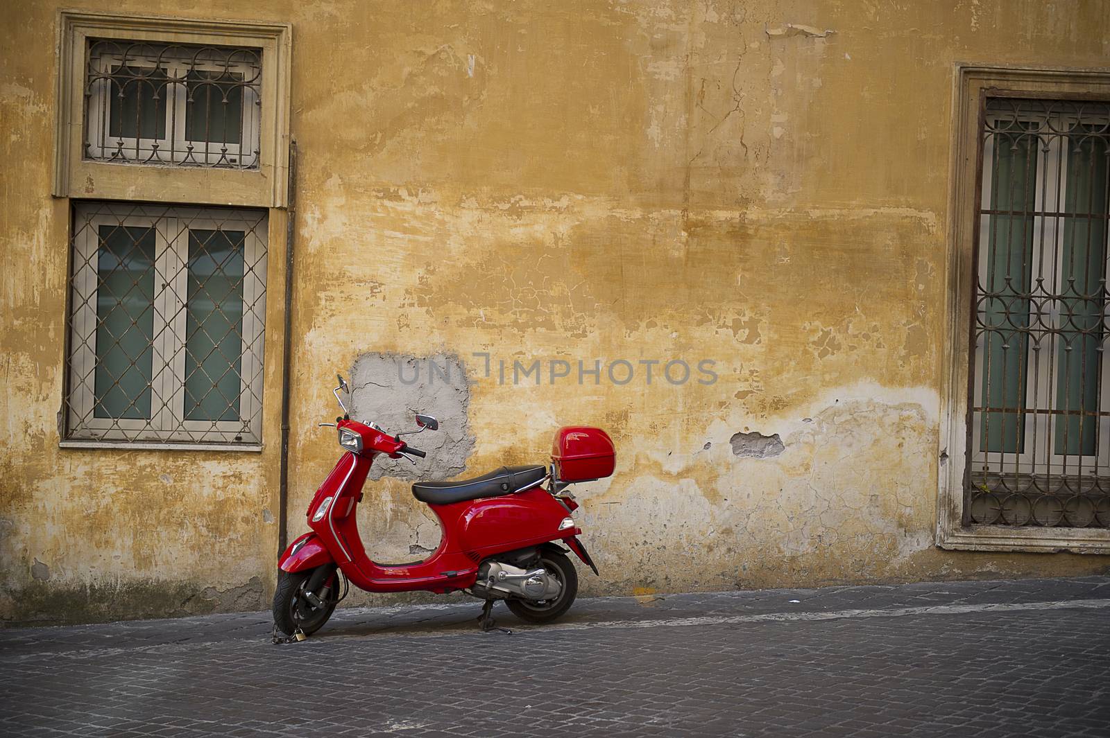 Bright red Vespa scooter parked in an urban street in front of a grungy old townhouse with burglar bars on the windows and crumbling plaster on the walls