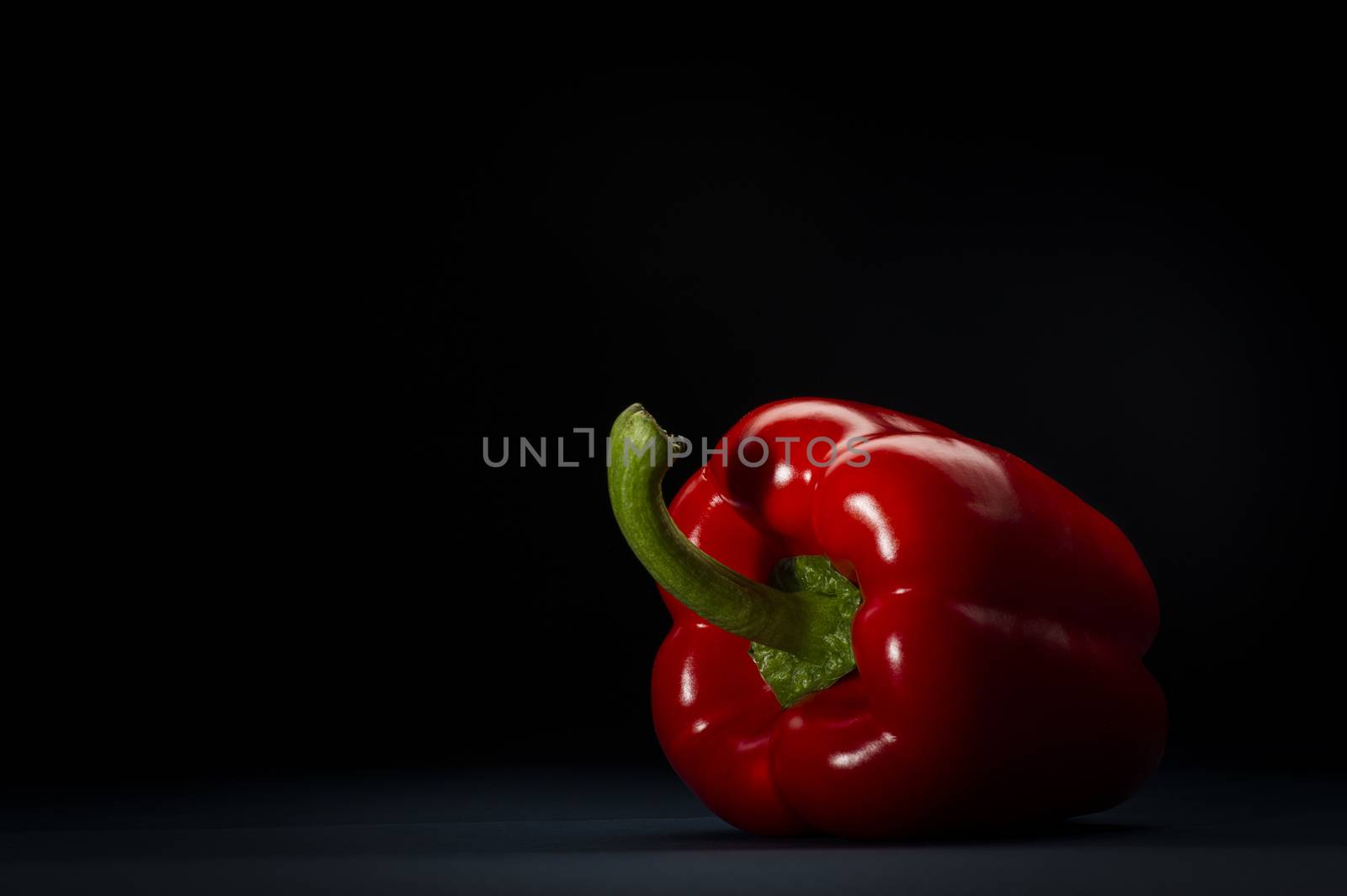 Fresh whole red bell pepper or capsicum rich in antioxidants and vitamin c used as a salad and cooking ingredient, viewed from the stalk end on a dark background with copyspace