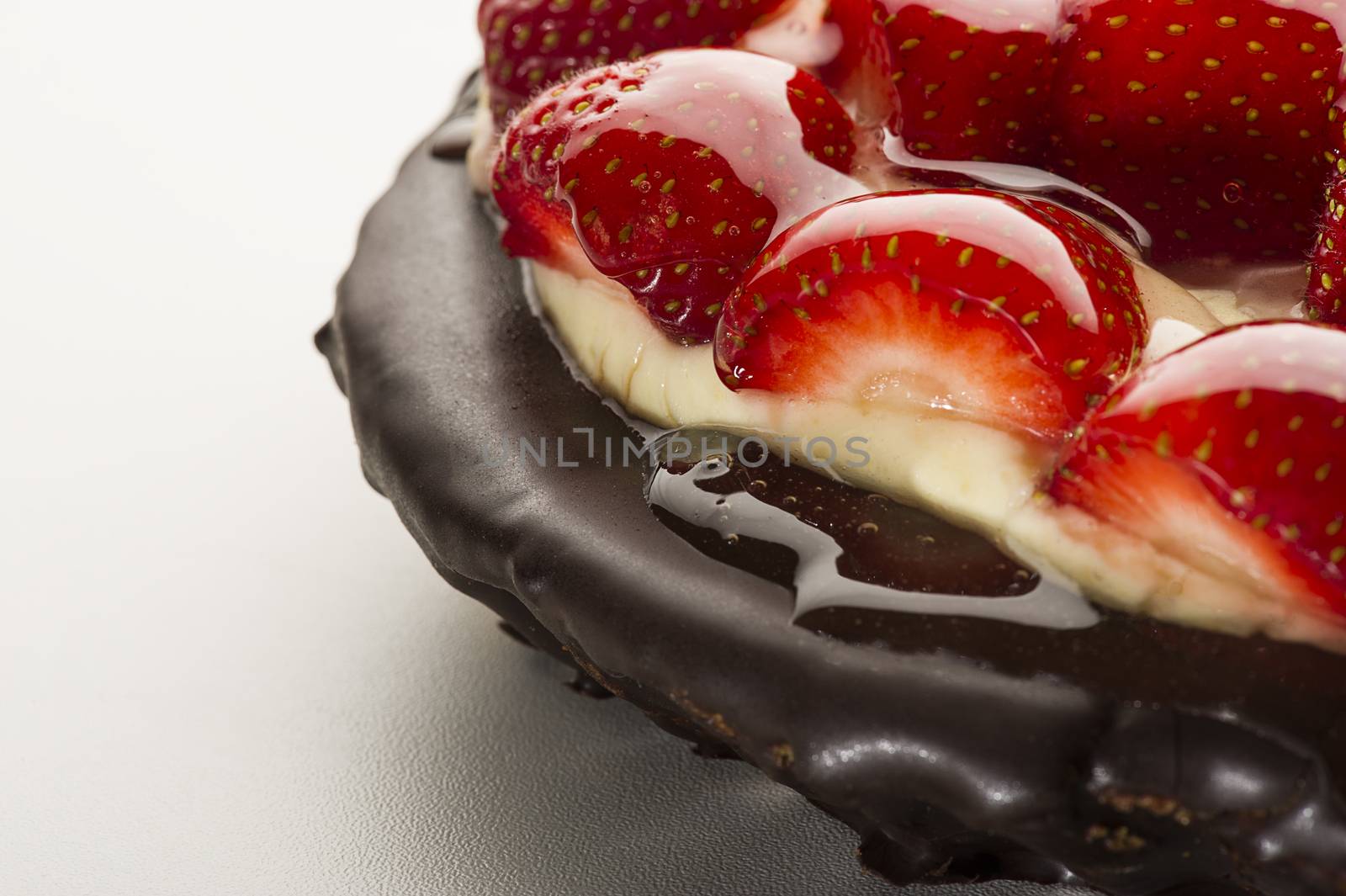 Closeup view of a freshly baked strawberry pie or tart with a topping of halved fresh ripe red berries glazed with syrup on a chocolate base, copyspace to the left