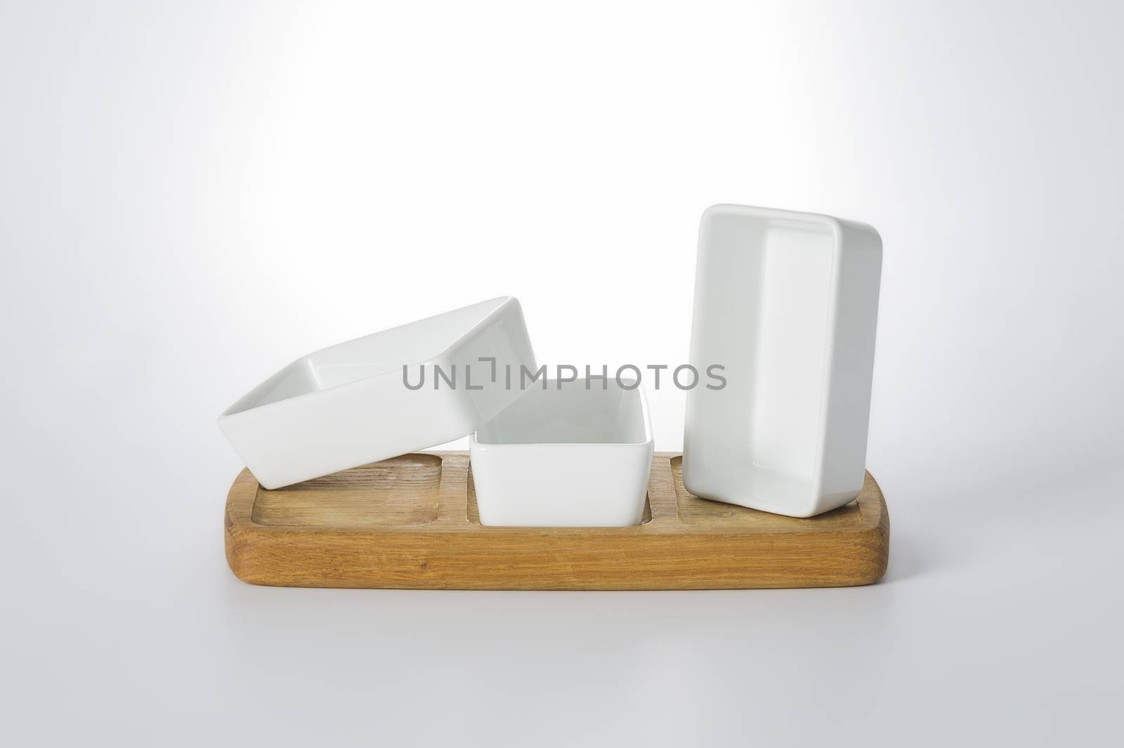 Set of three ceramic white rectangular dishes on a wooden fitted base for serving food or snacks artistically arranged in different orientations on a white background
