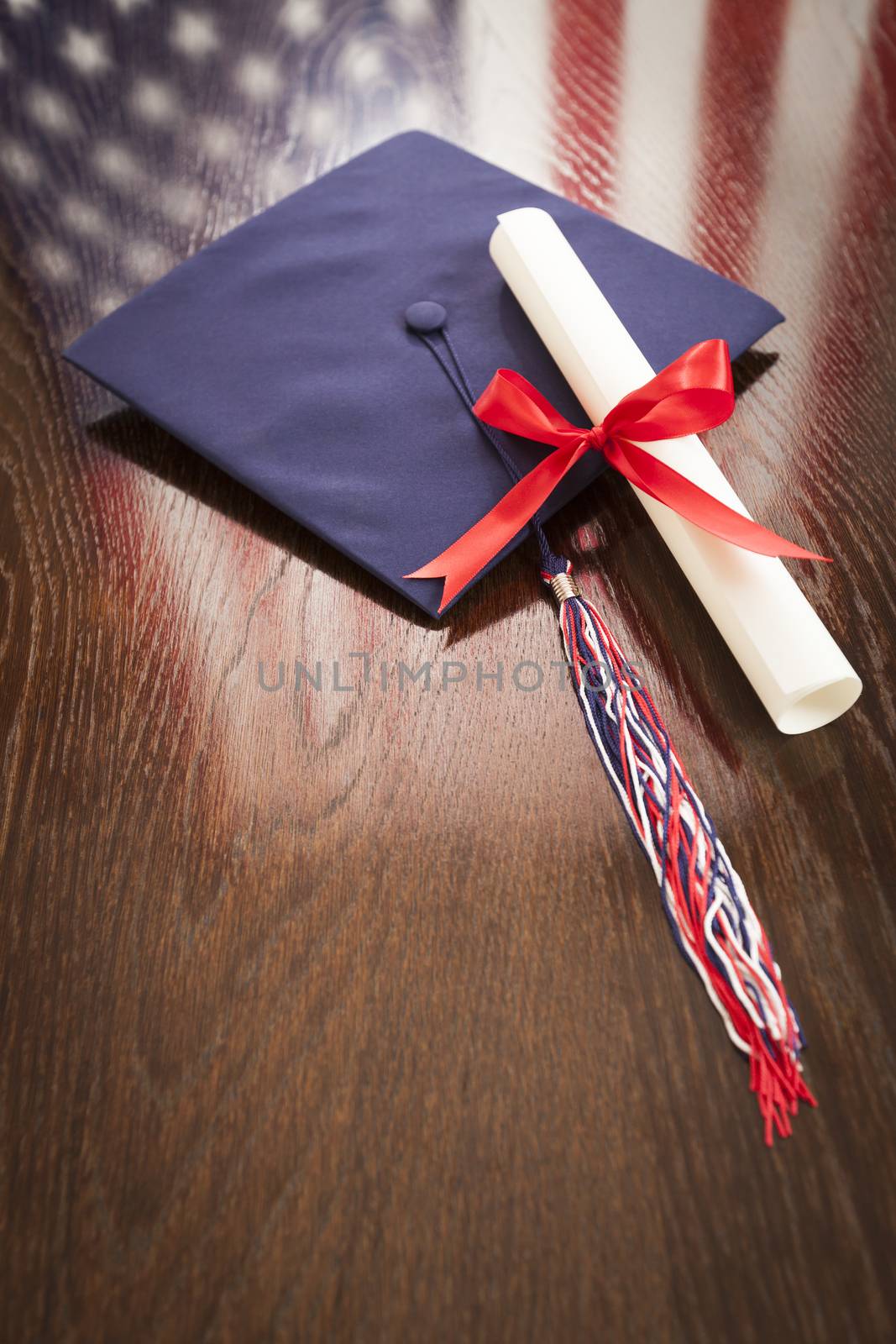 Graduation Cap with Tassel and Diploma Wresting on Wooden Table with American Flag Reflection.