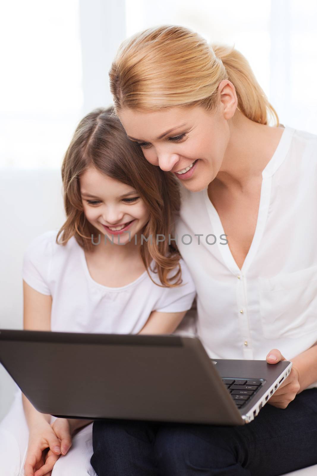 family, child, technology and home concept - smiling mother and little girl with laptop at home