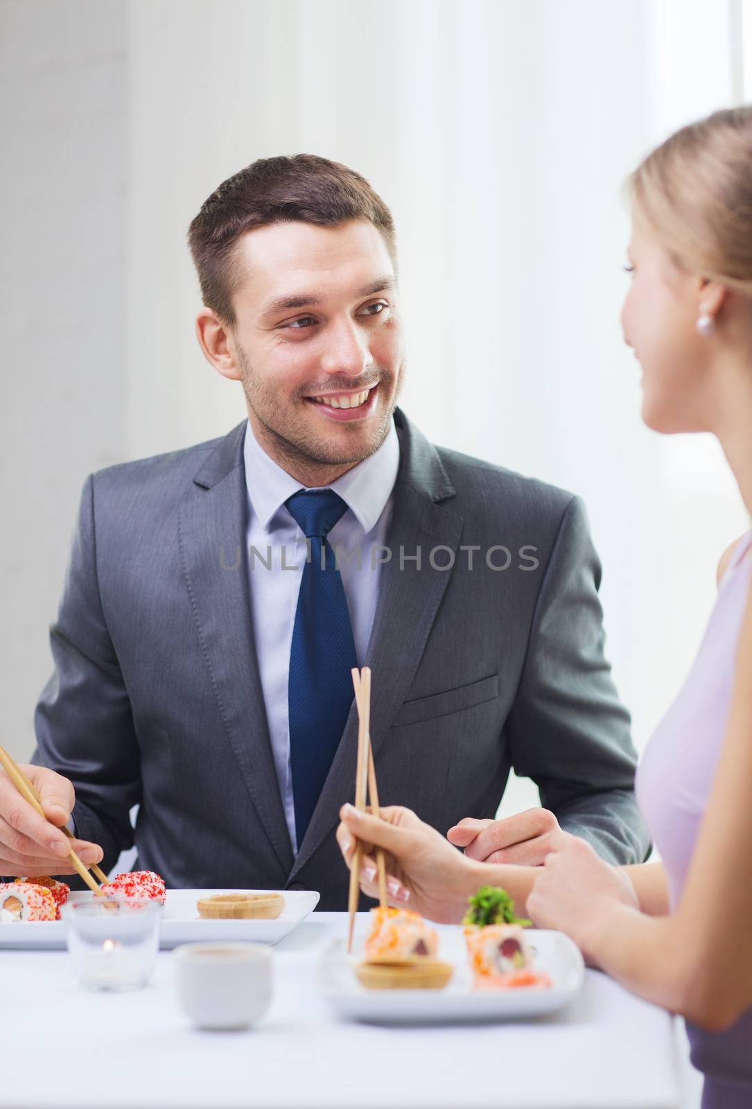 smiling couple eating sushi at restaurant by dolgachov