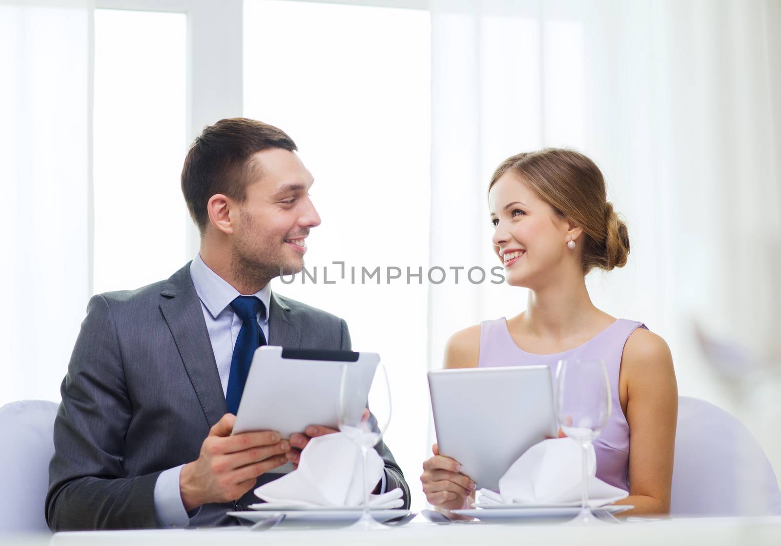 couple with menus on tablet pc at restaurant by dolgachov