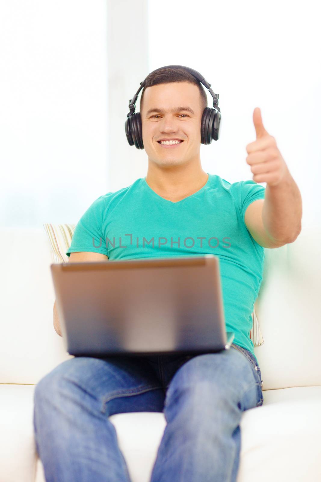 technology, home, music and lifestyle concept - smiling man with laptop and headphones at home showing thumbs up