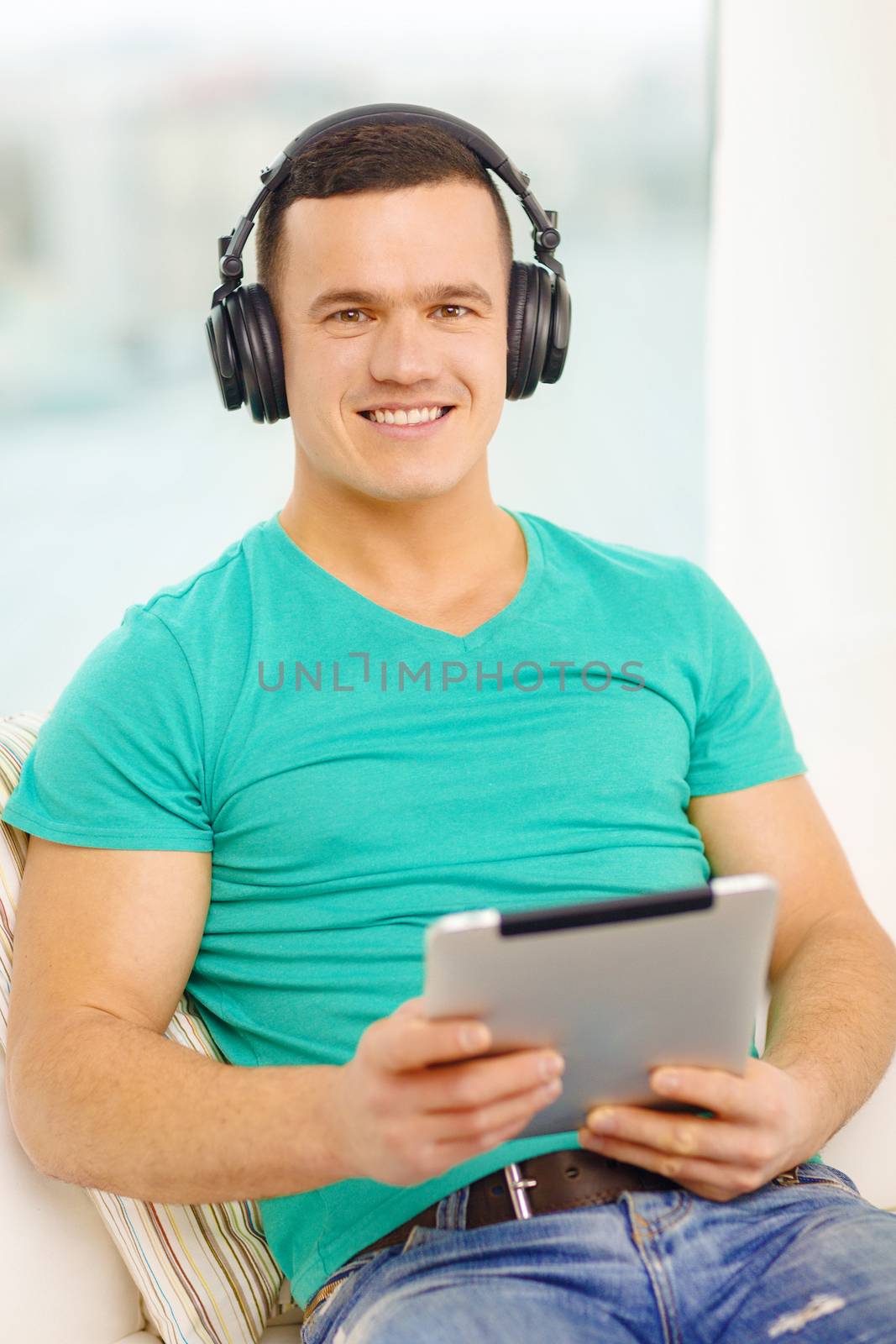 smiling man with tablet pc and headphones at home by dolgachov